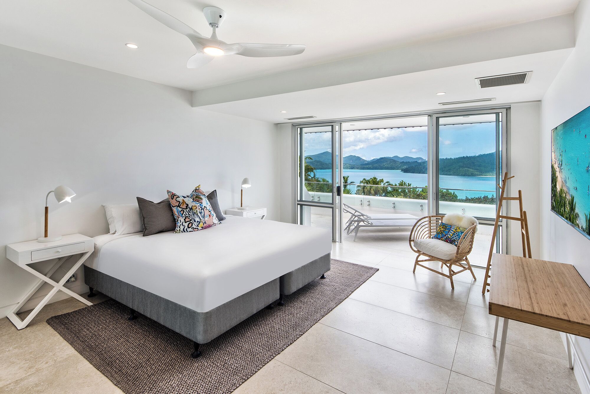 Un dormitorio moderno con una cama grande, un escritorio, una silla y vistas al mar.