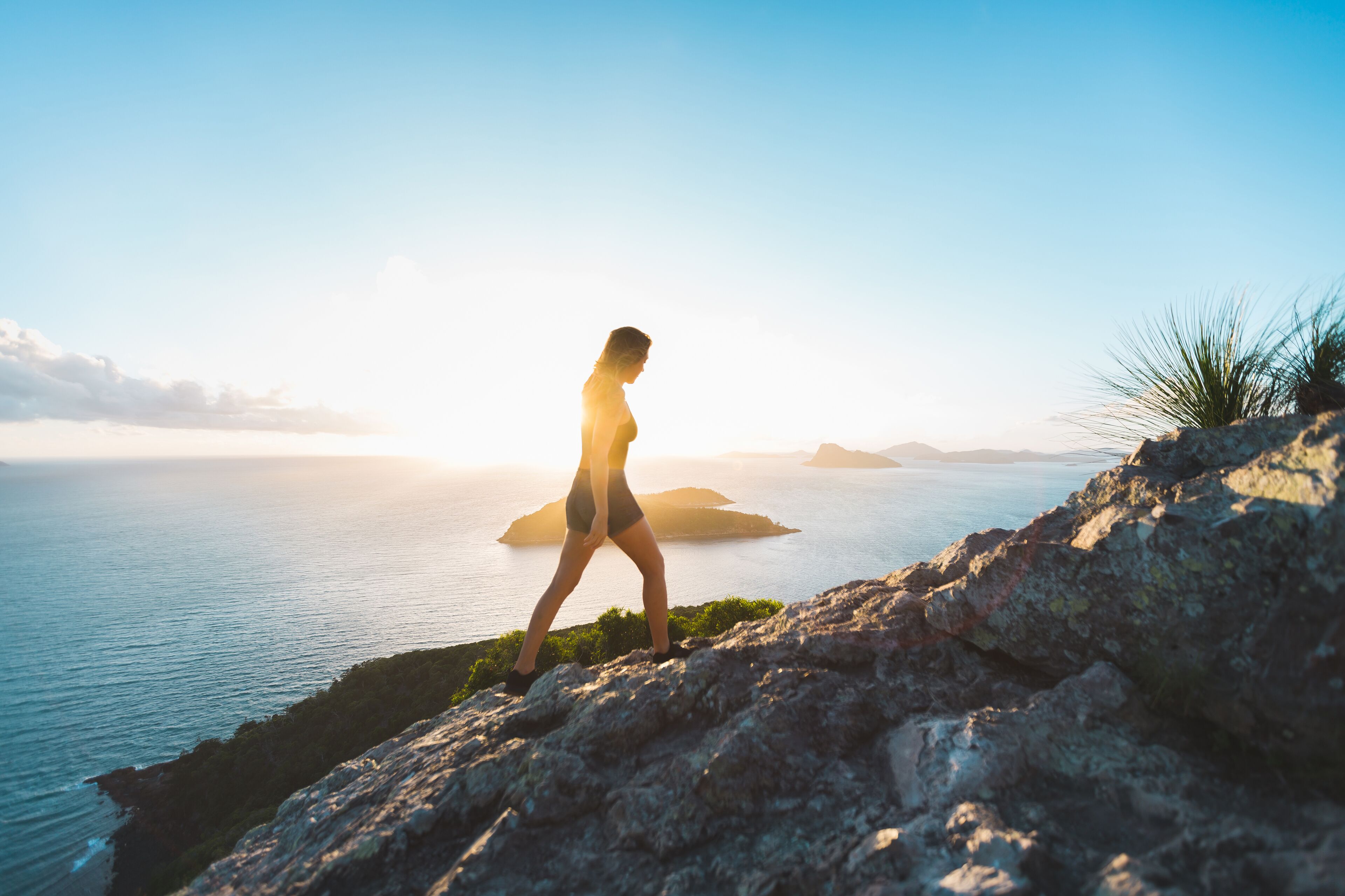 A person walking on a rocky path overlooking a body of water with islands in the distance.