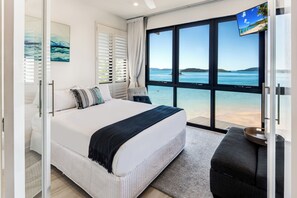 A bedroom with a large bed, a sofa, a TV, and a view of the sea. - Hamilton Island Holiday Homes (Whitsundays)