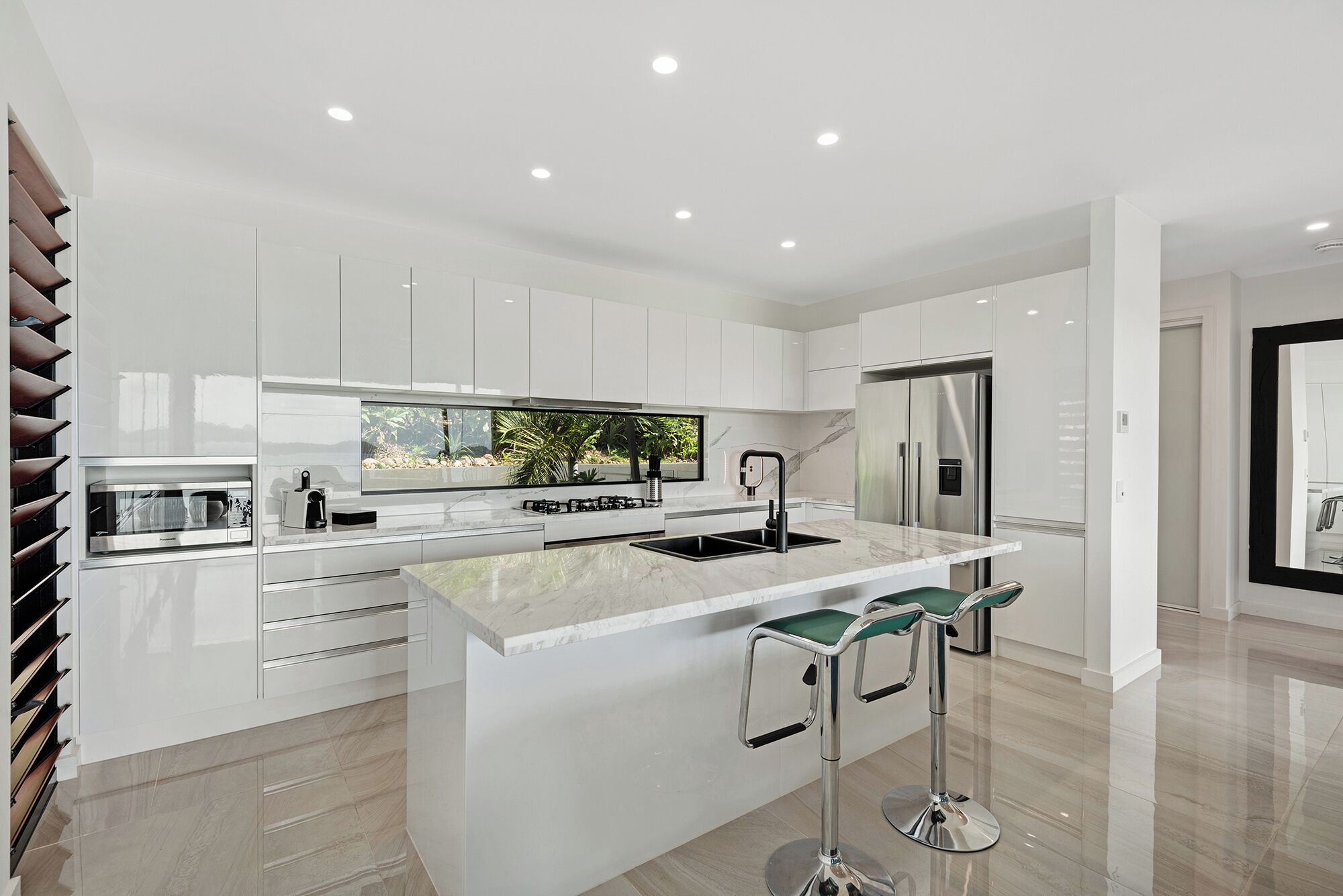 A modern kitchen with white cabinetry, a large island with bar stools, a built-in oven, and a stainless steel refrigerator.