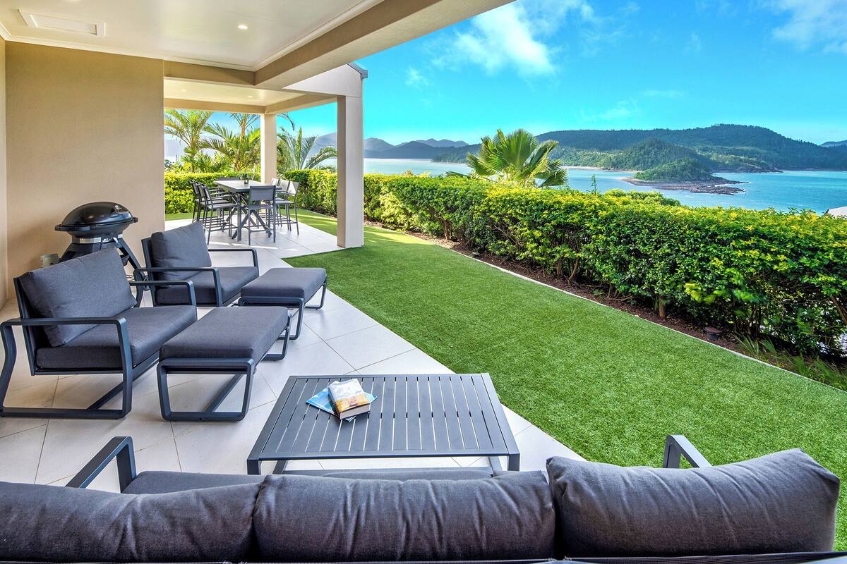 A patio with outdoor furniture, a grill, and a view of the ocean.