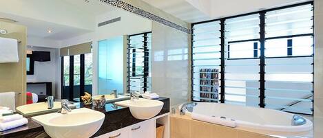 A modern bathroom with two sinks, a large mirror, a bathtub, and a view of the outdoors.