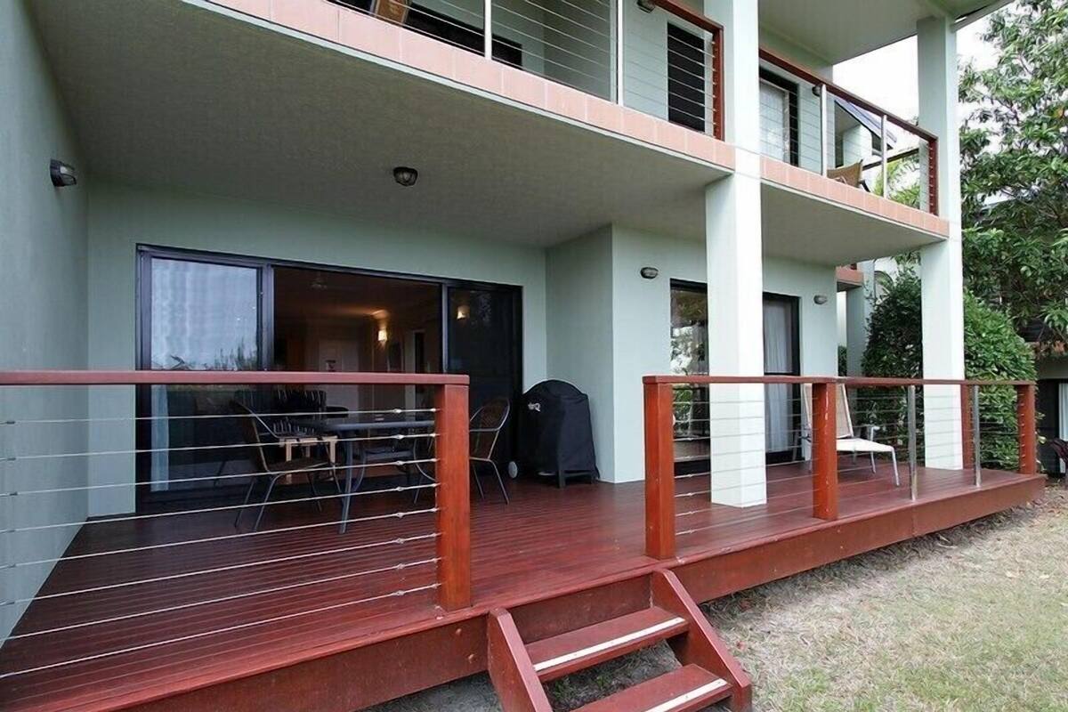 A multi-story residential building with a wooden deck, outdoor seating, and a covered area.