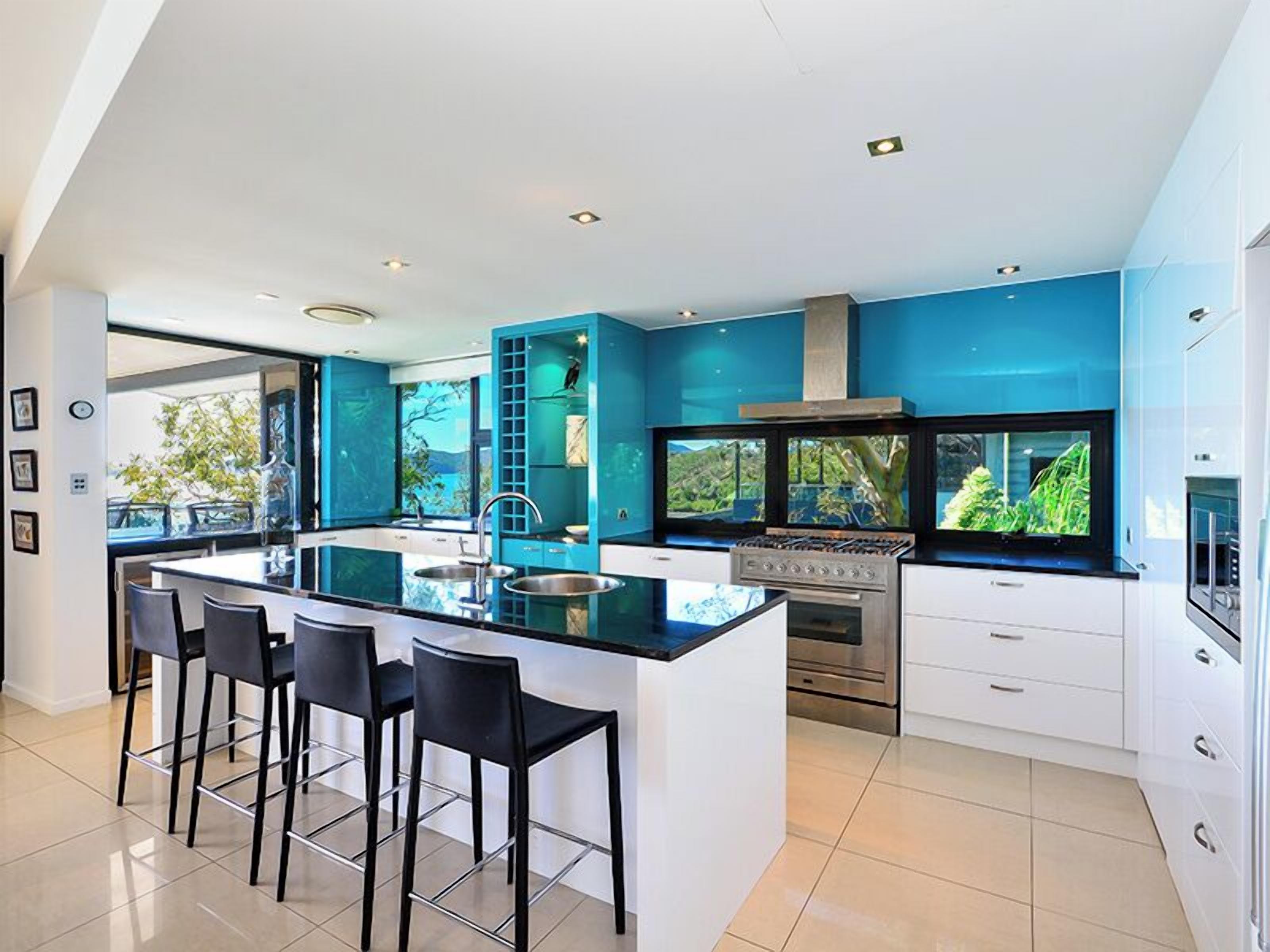 A modern kitchen with a central island, bar stools, a stove, and a large window.