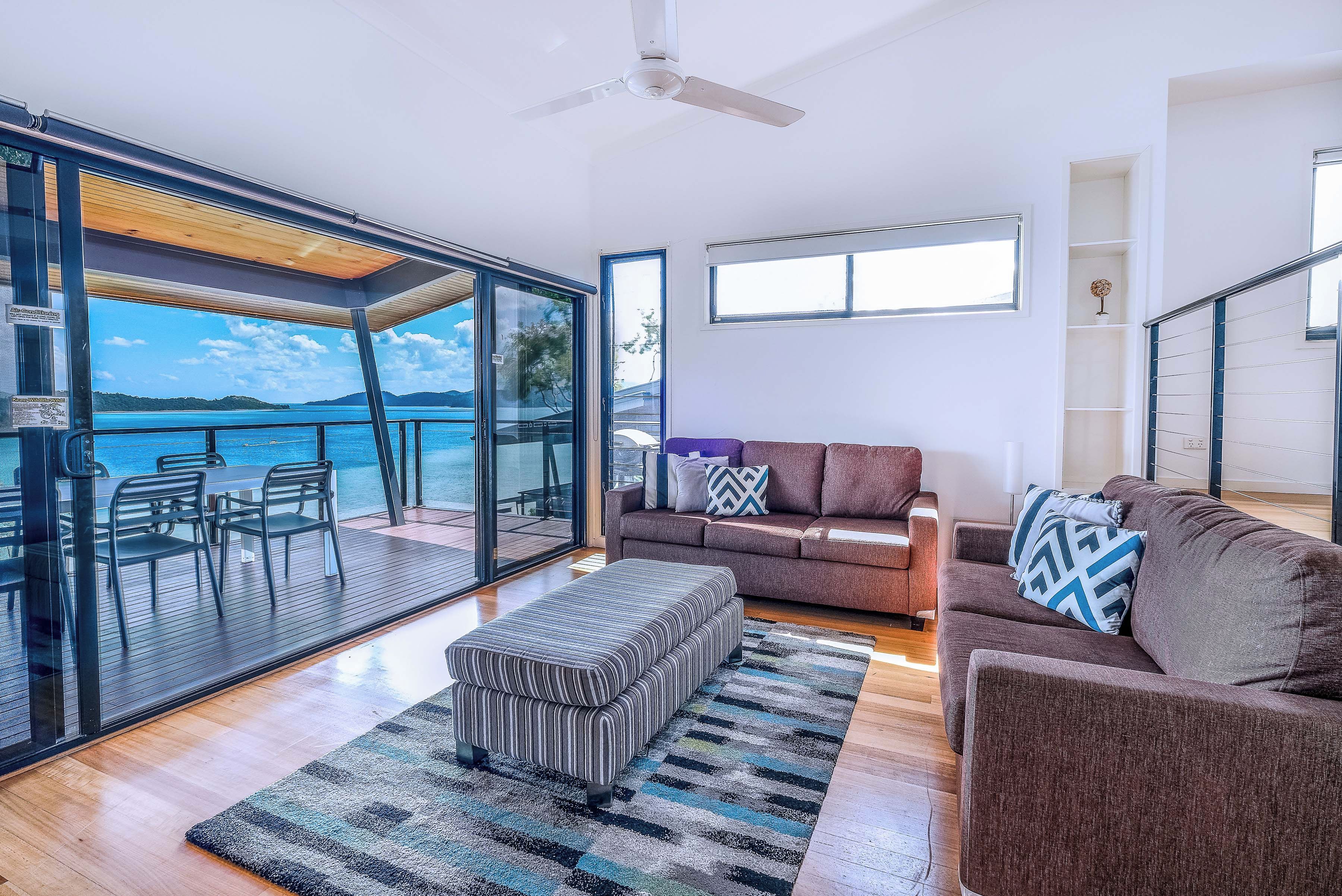 A modern living room with a large sliding glass door leading to a balcony overlooking a body of water.