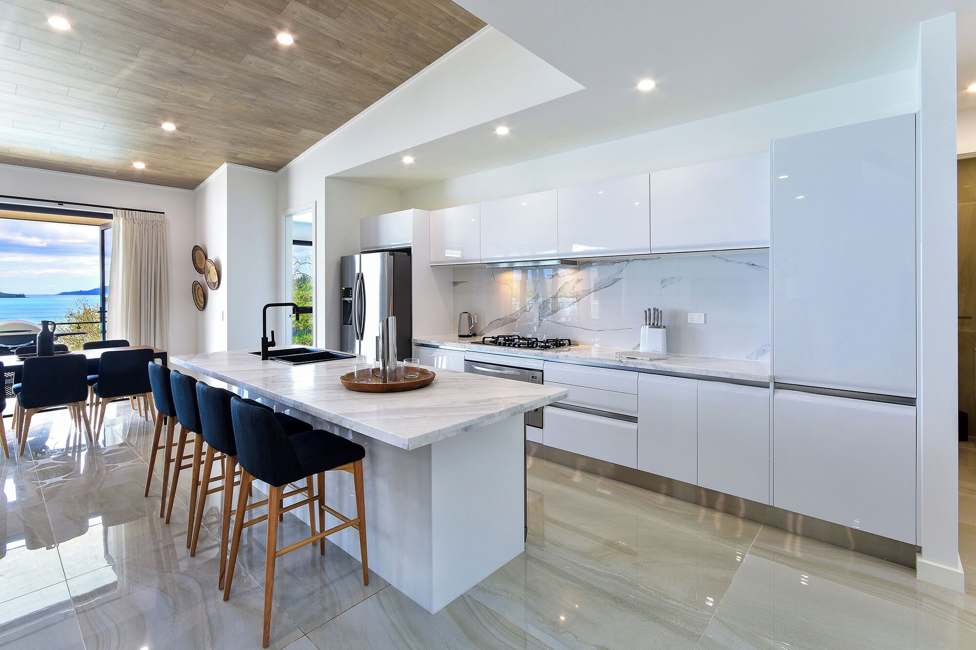 A modern kitchen with white cabinetry, a central island with bar stools, a stainless steel refrigerator, and a gas stove.