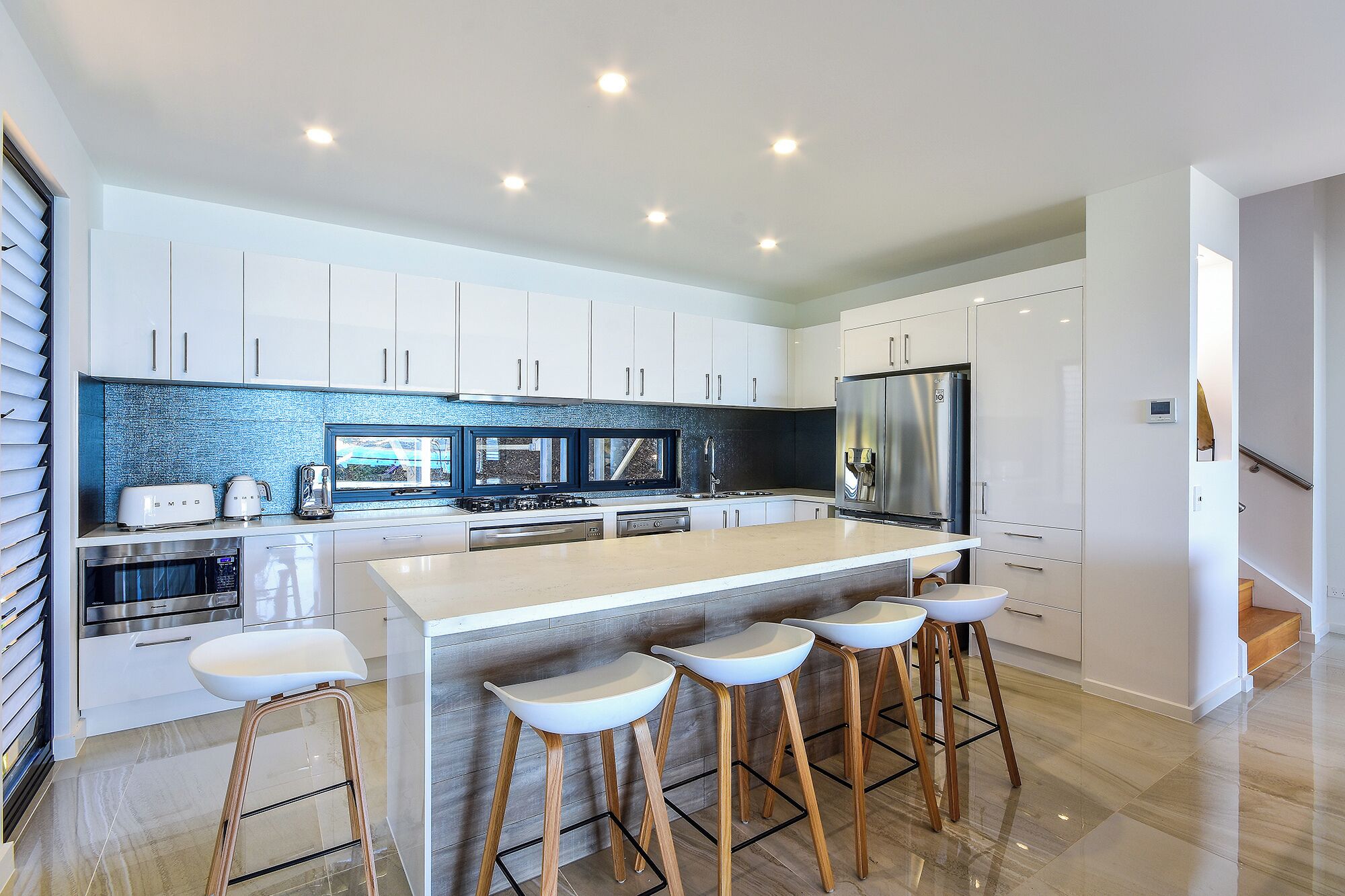 A modern kitchen with white cabinets, a central island with stools, stainless steel appliances, and a backsplash with a blue and black pattern.