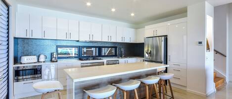 A modern kitchen with white cabinets, a central island with stools, stainless steel appliances, and a backsplash with a blue and black pattern.