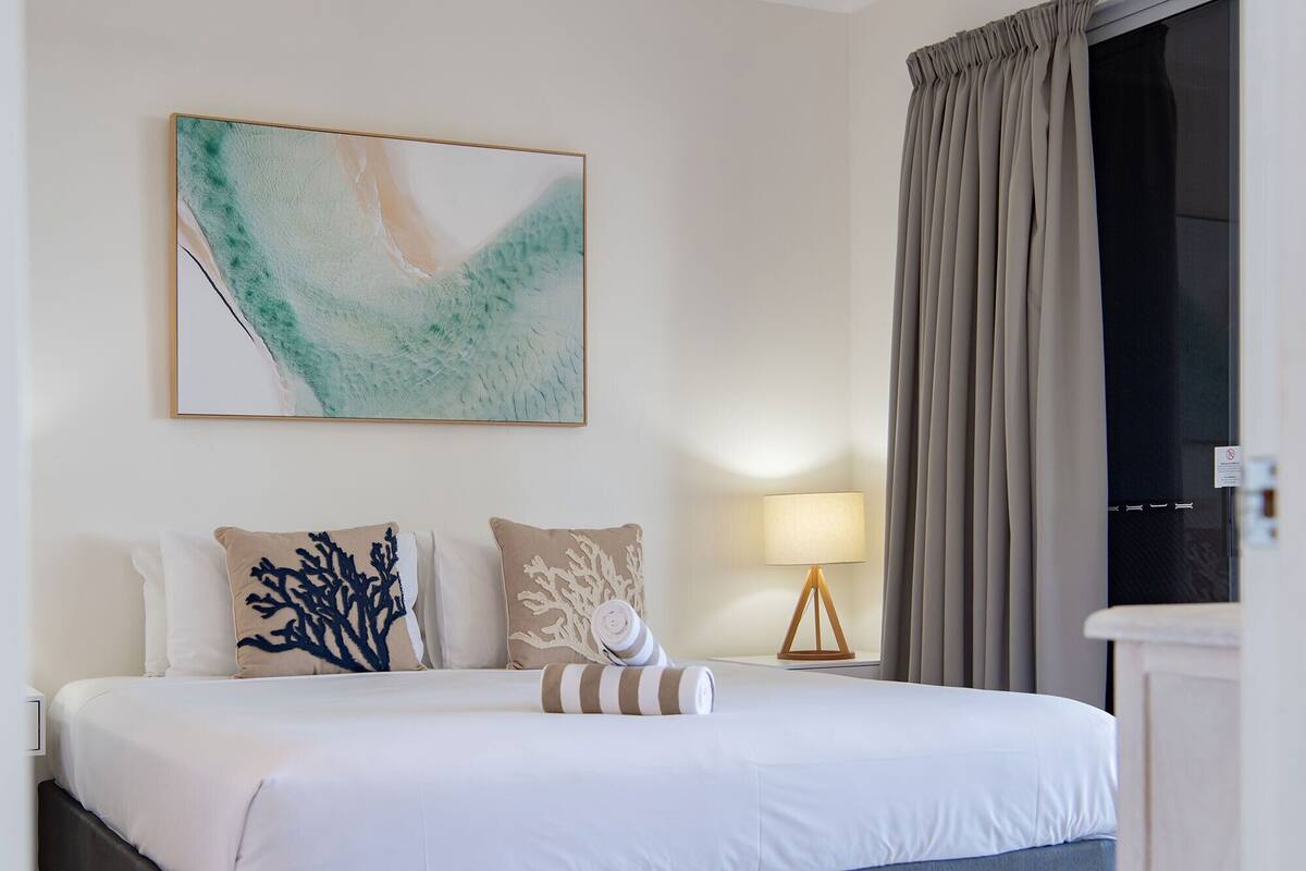 A hotel room with a bed, a painting, a lamp, and curtains.