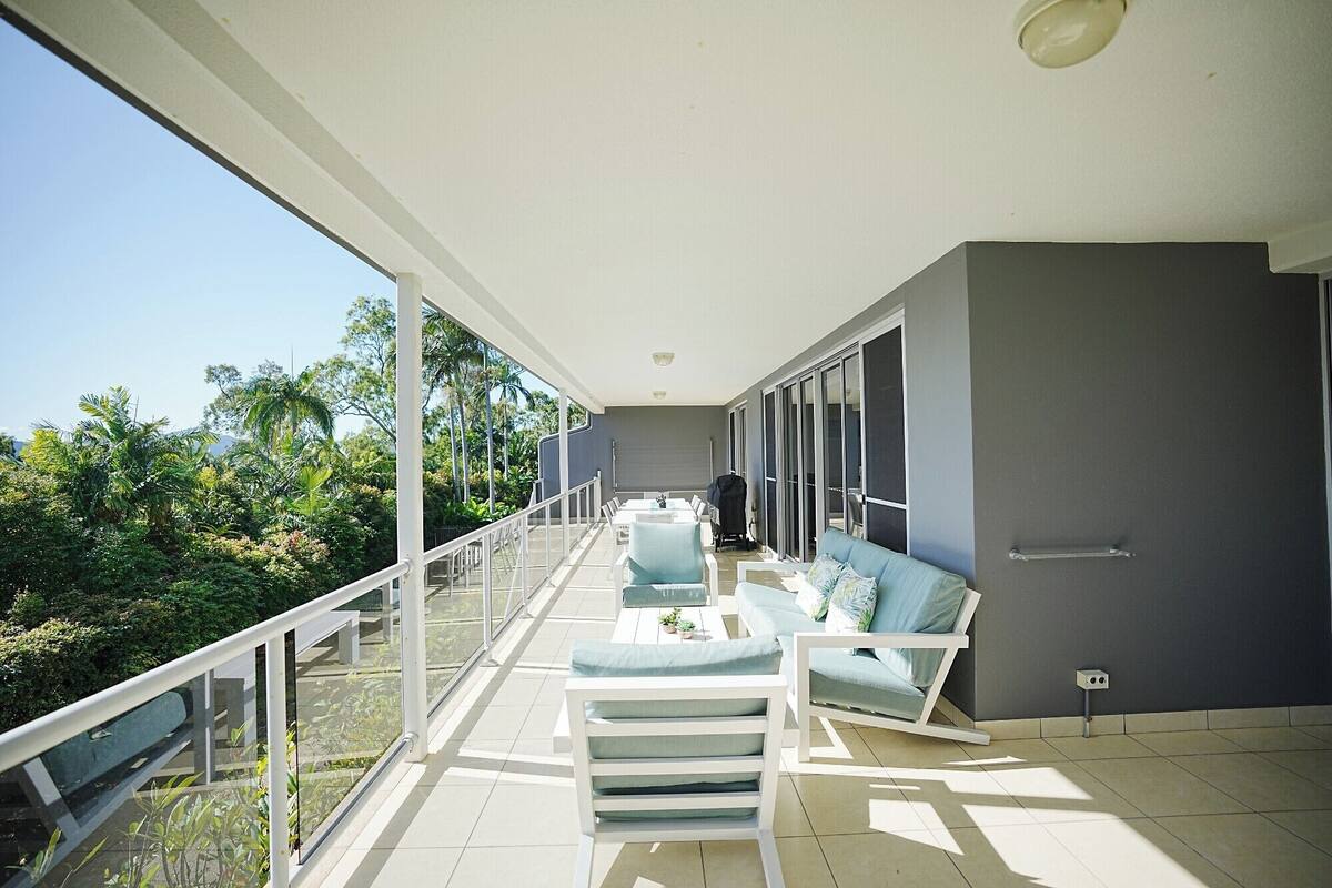 A balcony with a sofa and chairs, a railing, and a view of greenery.