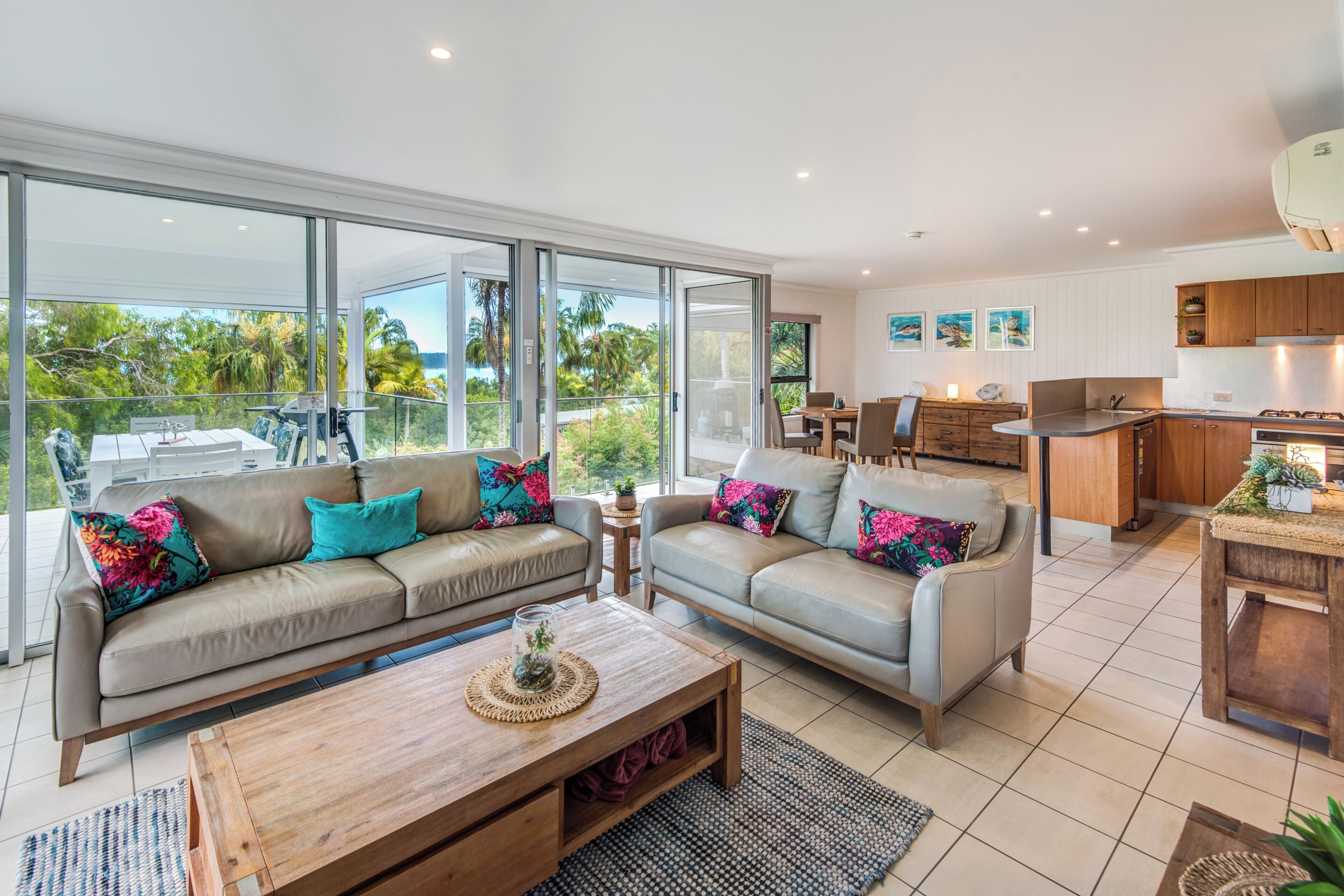 A modern living room with two sofas, a coffee table, and a kitchen area with wooden cabinets.