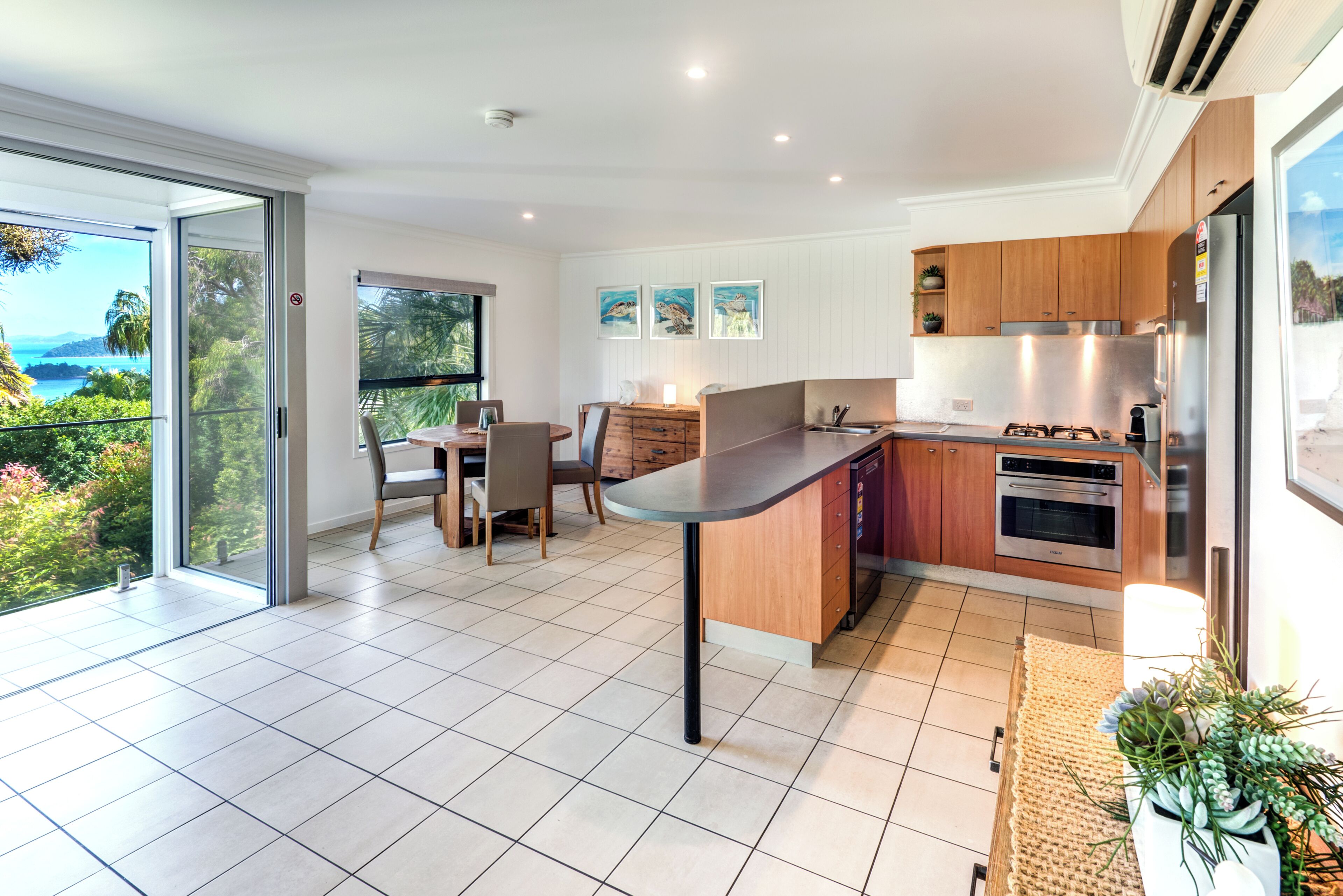 A modern kitchen with a dining area, large windows, and a view of the outdoors.