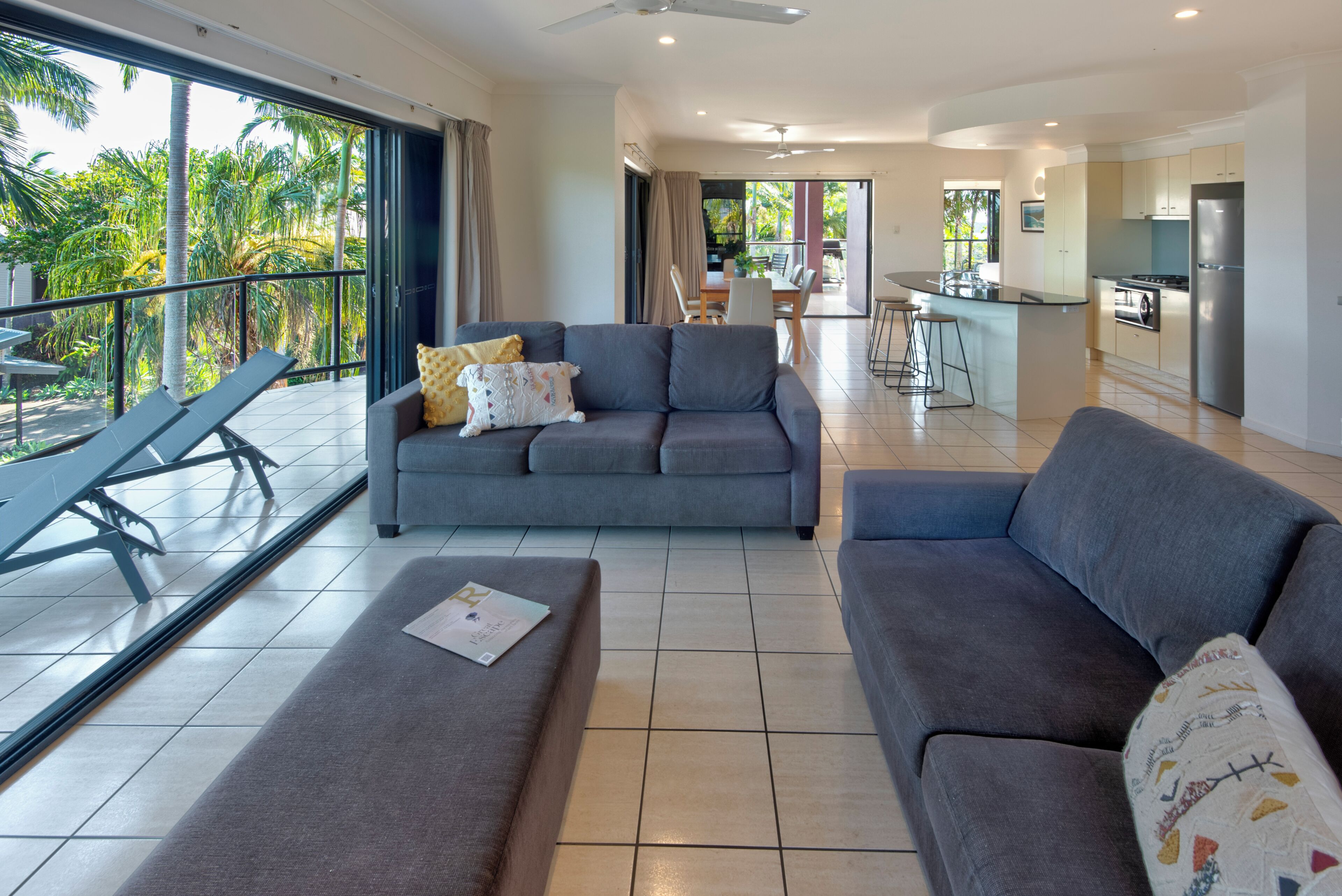A modern living area with a sofa, a dining table, and a kitchen in the background.