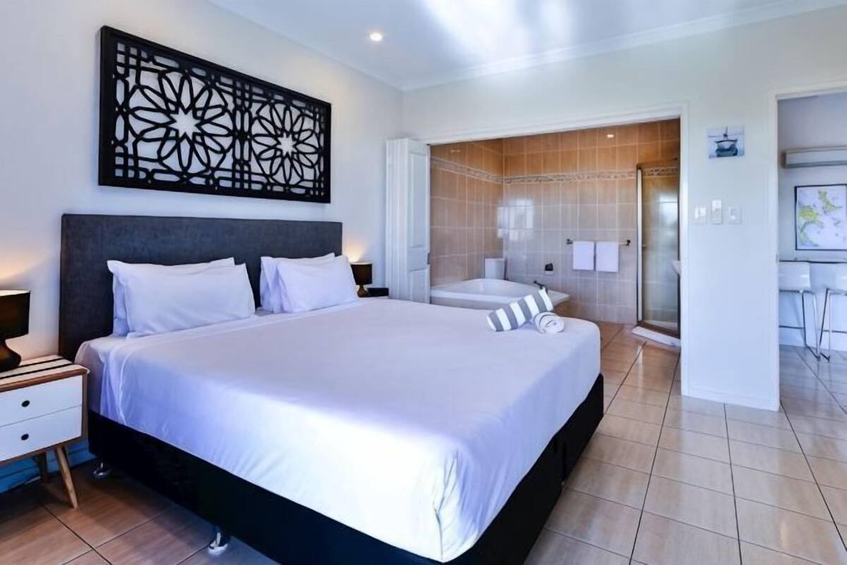 A hotel room with a large bed, a bathroom with a shower, and a small kitchenette.