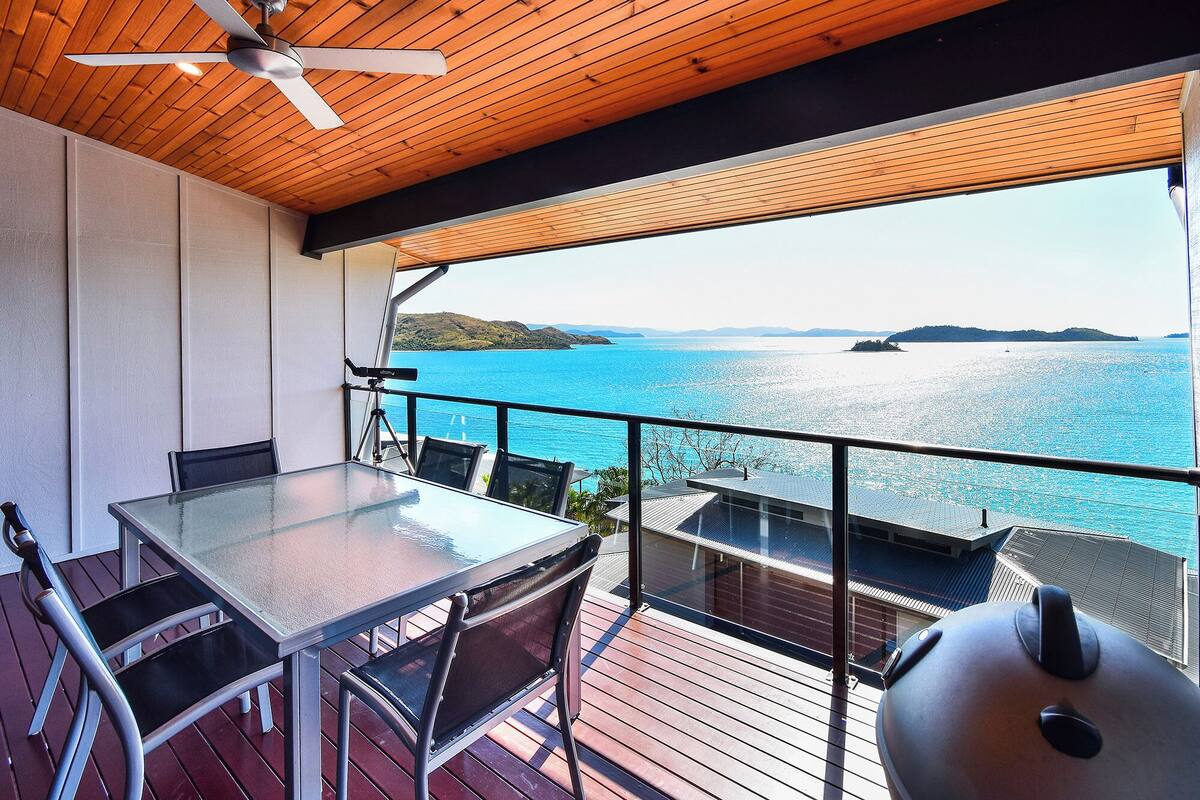 A balcony with a table and chairs, a ceiling fan, and a view of the sea.