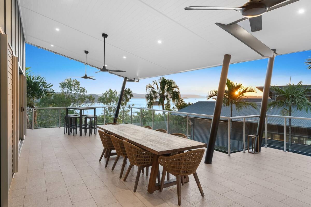 A covered outdoor dining area with a table and chairs, ceiling fans, and a view of the sea.
