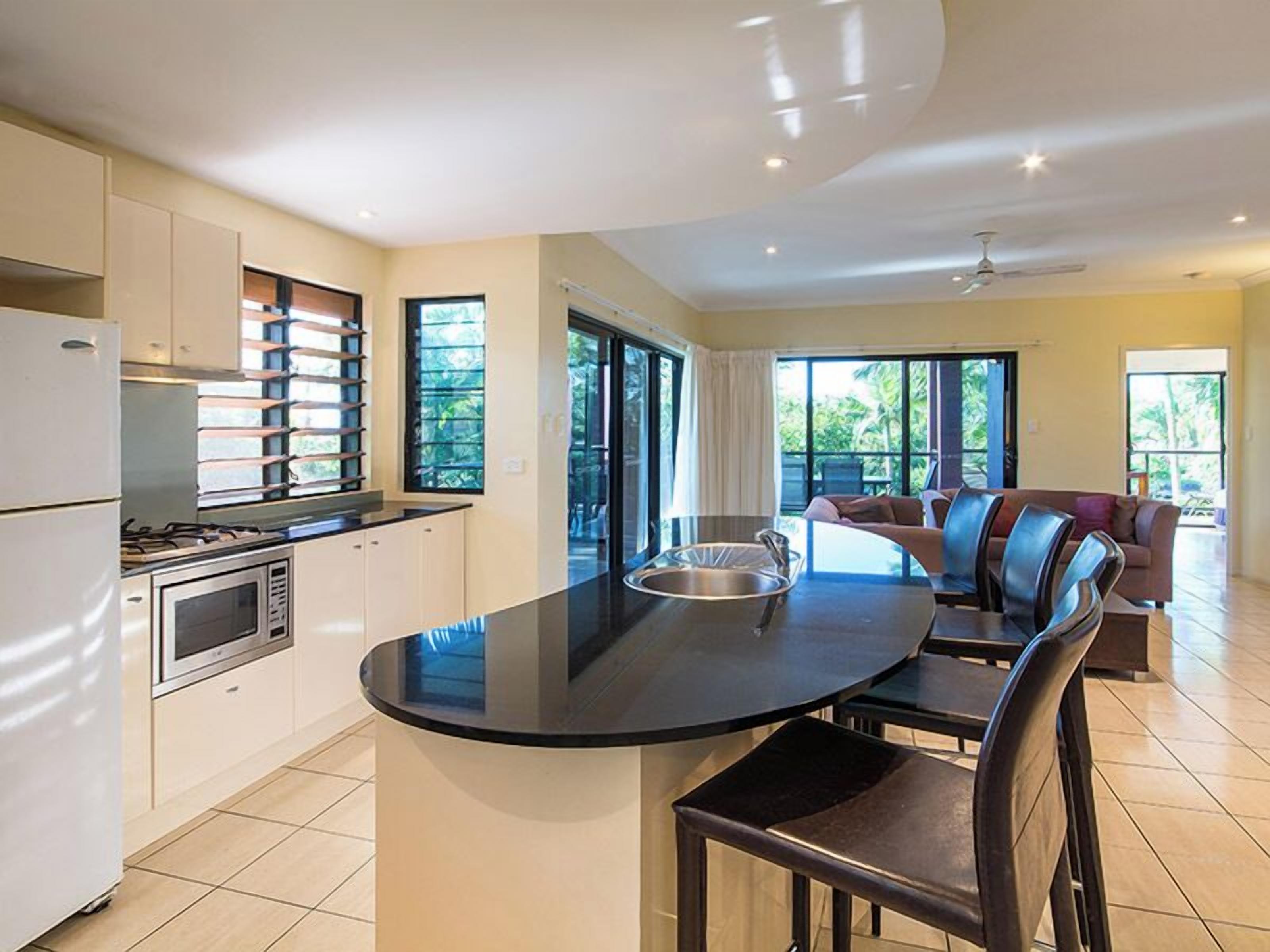 A modern kitchen with a central island, a dining area with chairs, and a sofa.