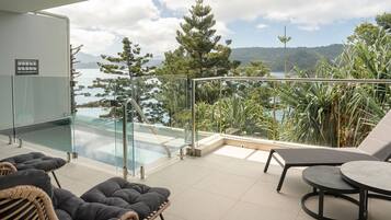 Un balcon doté d’une balustrade en verre, une piscine, des fauteuils en osier, une table et une vue sur la mer et les arbres.
