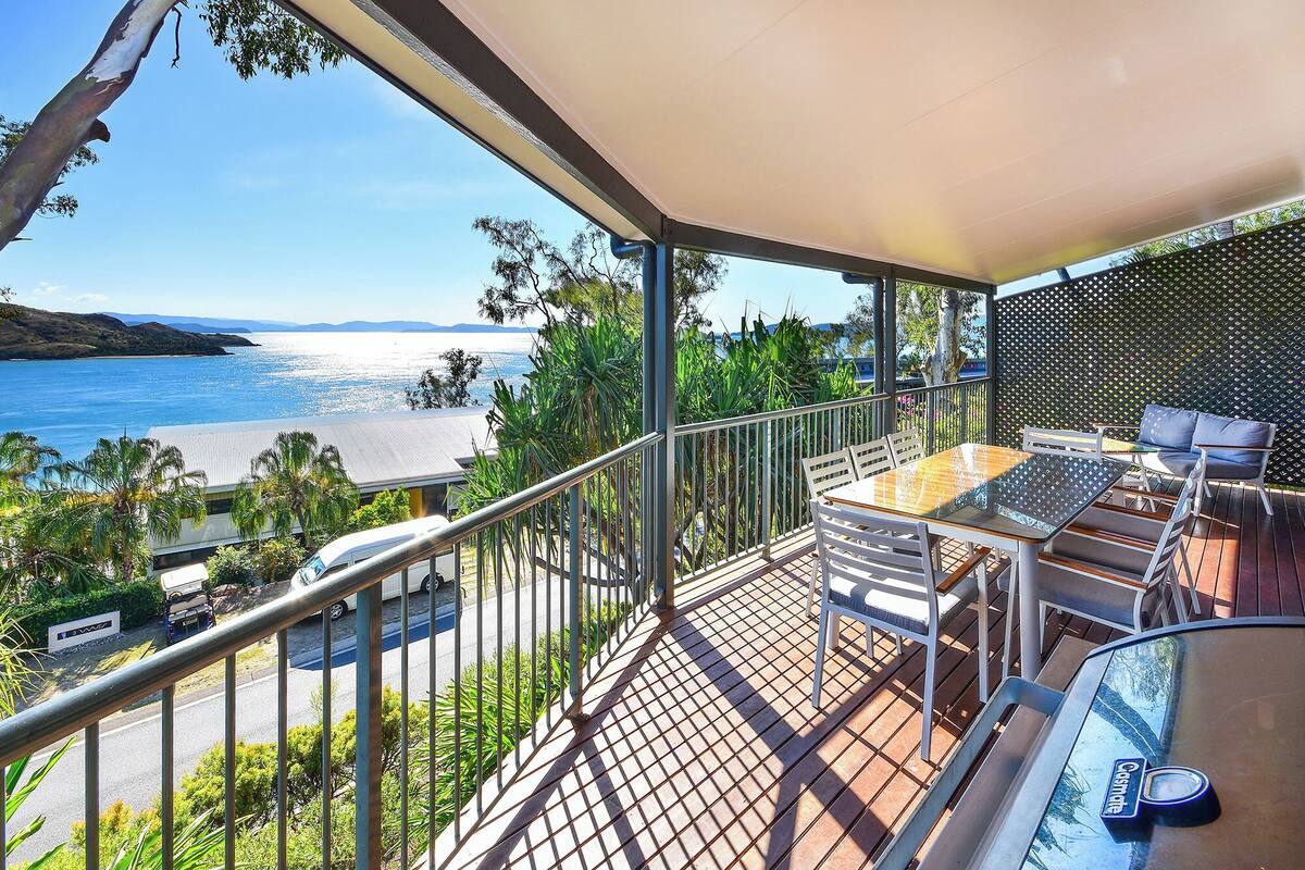 A balcony with a table and chairs, overlooking a beach and the sea.