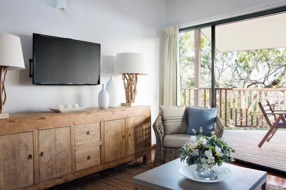 A living room with a wooden cabinet, a flat-screen TV, two lamps, a sofa, and a coffee table with flowers.