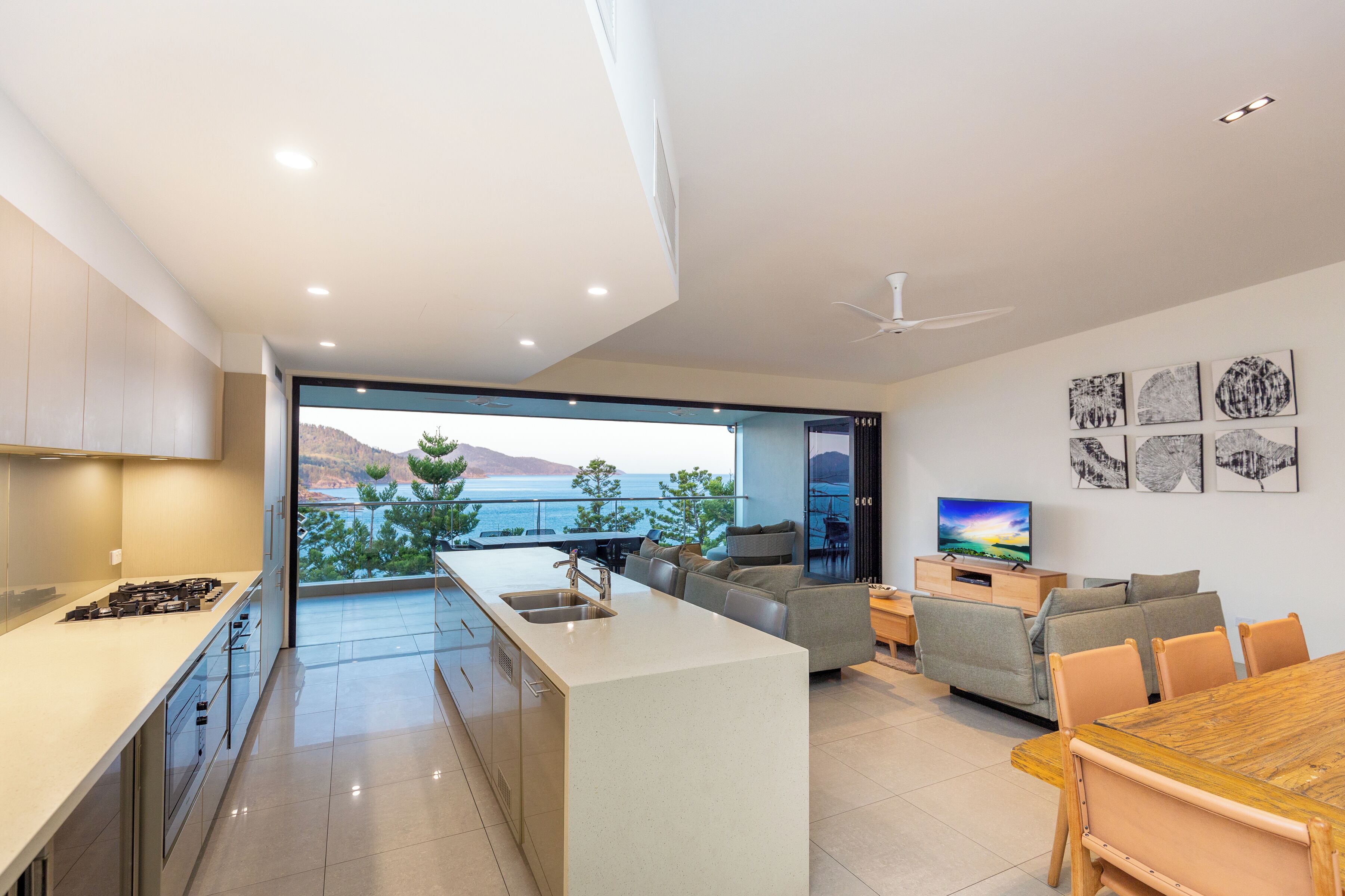 A modern kitchen with a large island, a dining area with a wooden table, and a living space with a sofa and TV.