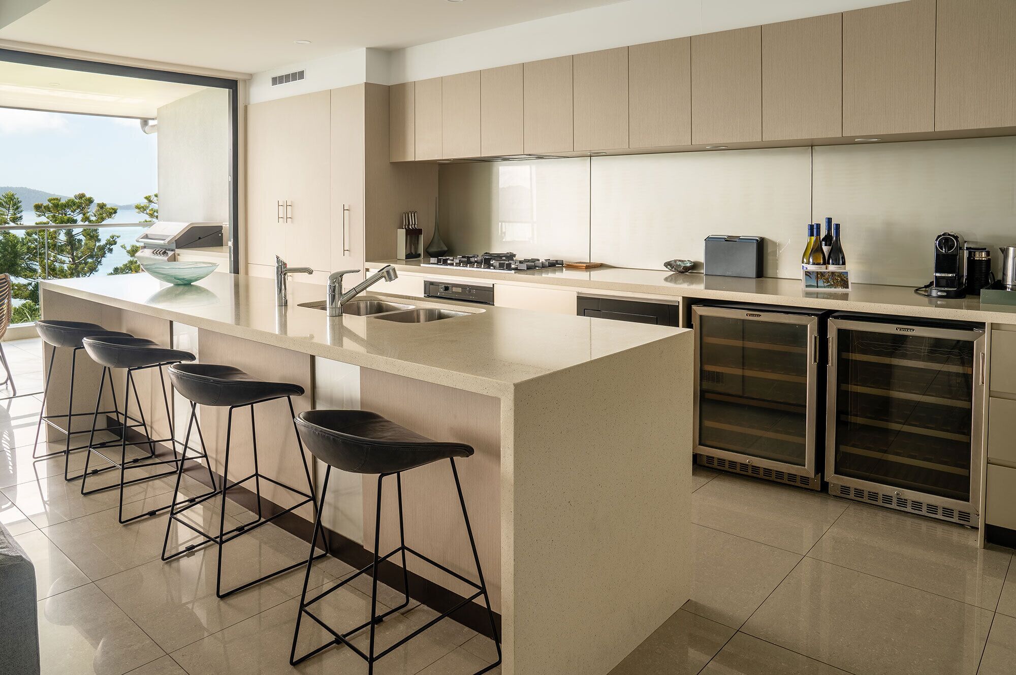 Una cocina moderna con una isla grande, taburetes de bar, electrodomésticos de acero inoxidable y vistas al exterior.