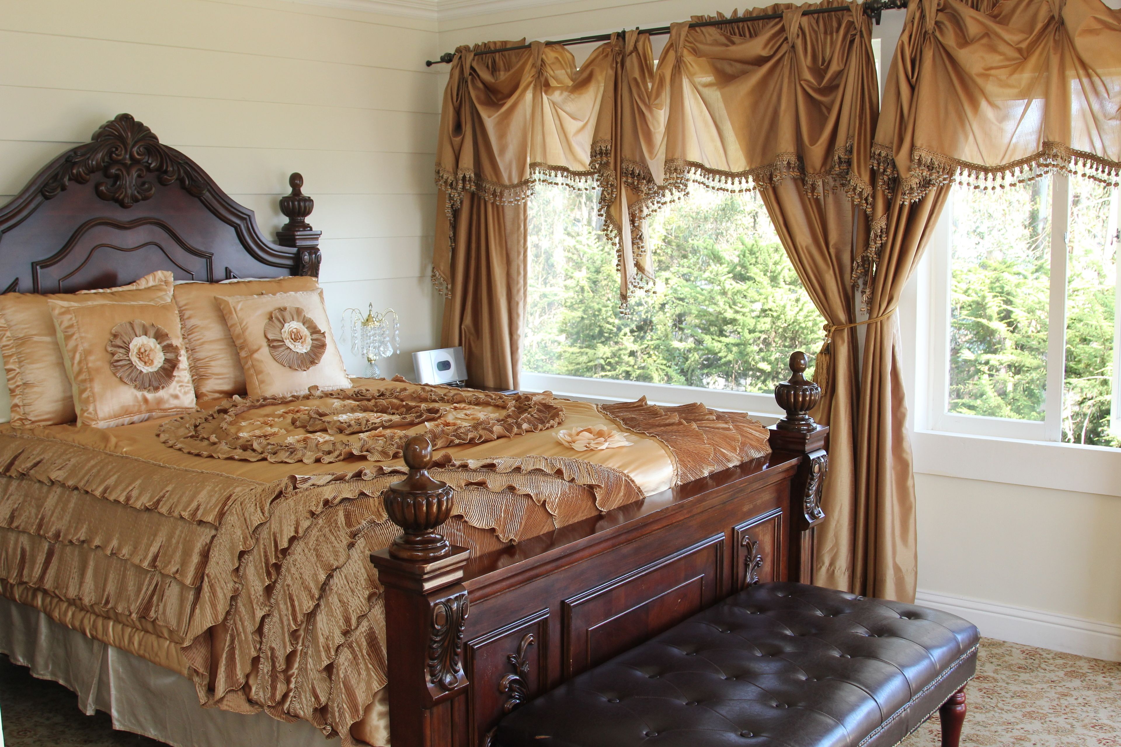A bedroom with a large bed, ornate headboard, and a view of greenery through the window.