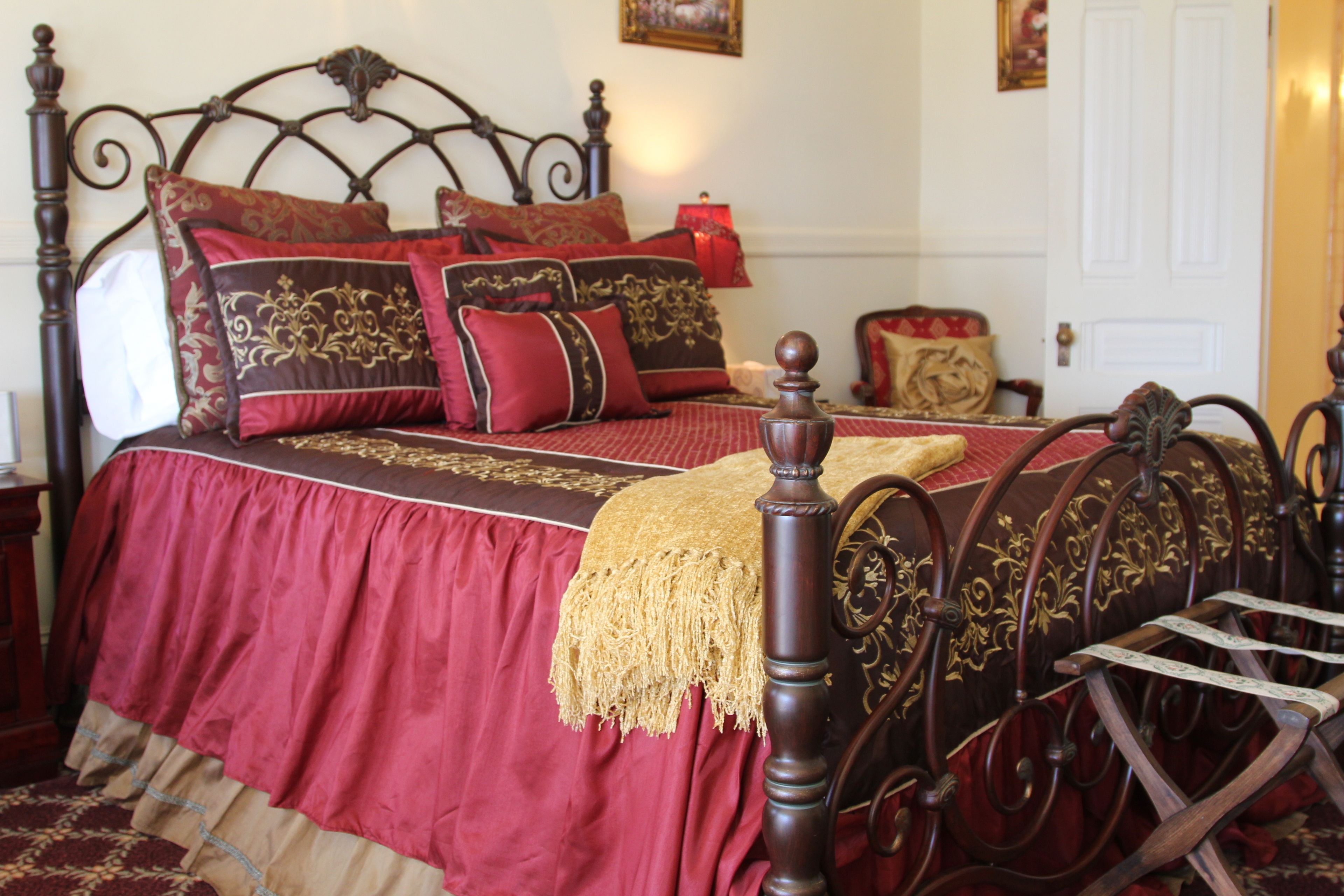 A traditional bed with a dark headboard, multiple pillows, and a red bedspread.