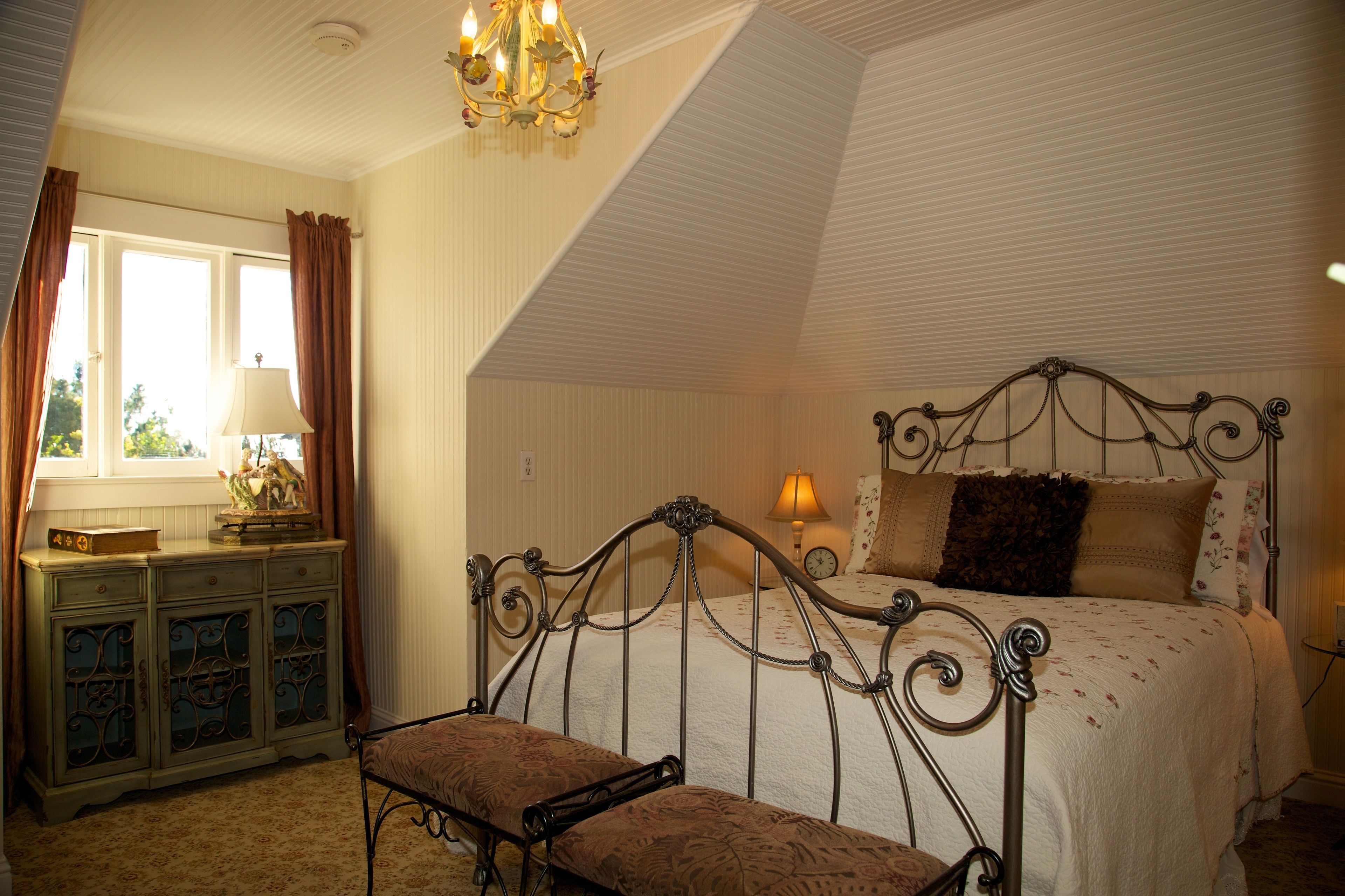A bedroom with a bed, a bench, a dresser, and a window with curtains.