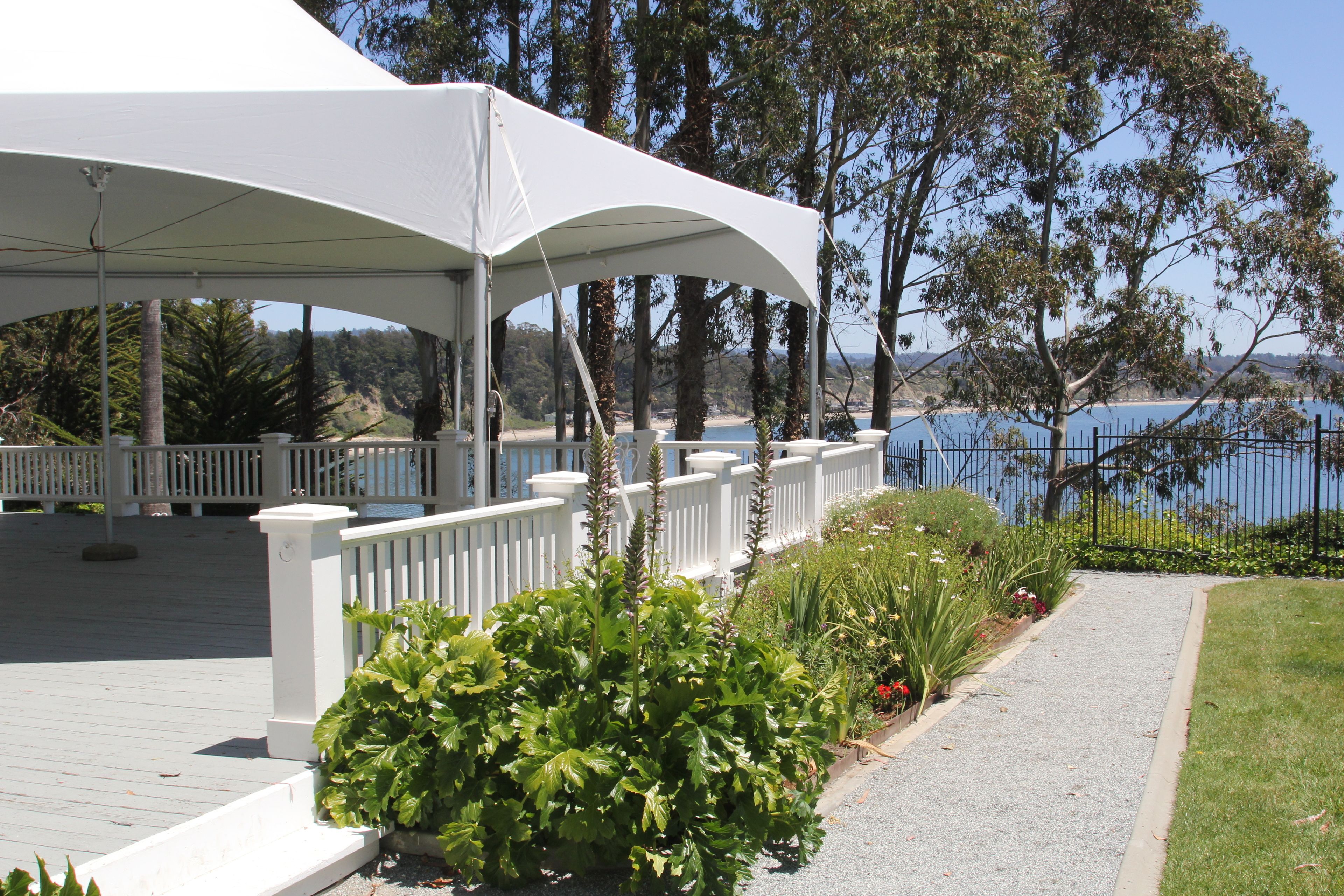 A covered outdoor area with a white railing, a gravel path, and lush greenery.
