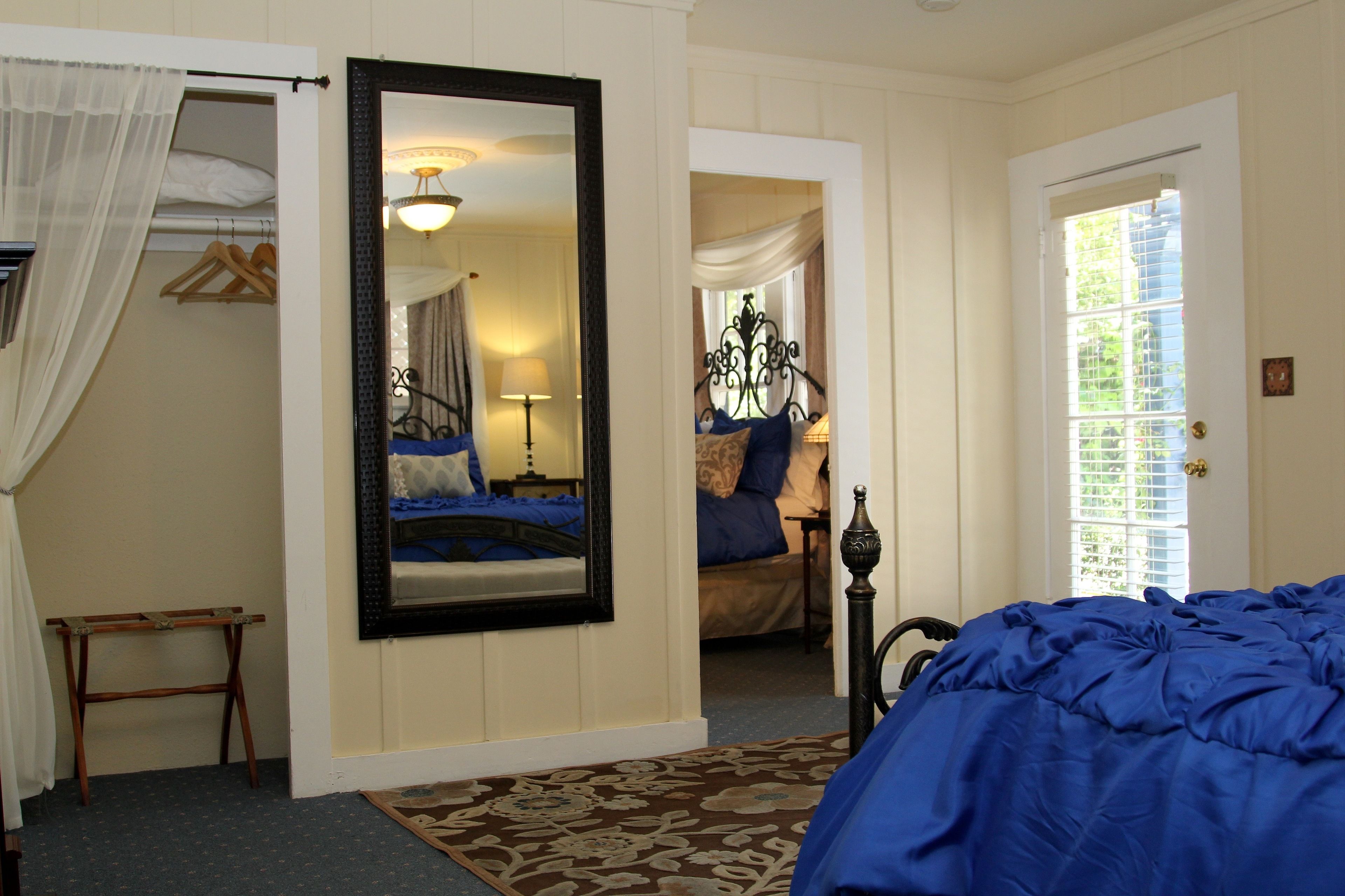 A bedroom with a large bed, a mirror, a wardrobe, and a door leading to another room.
