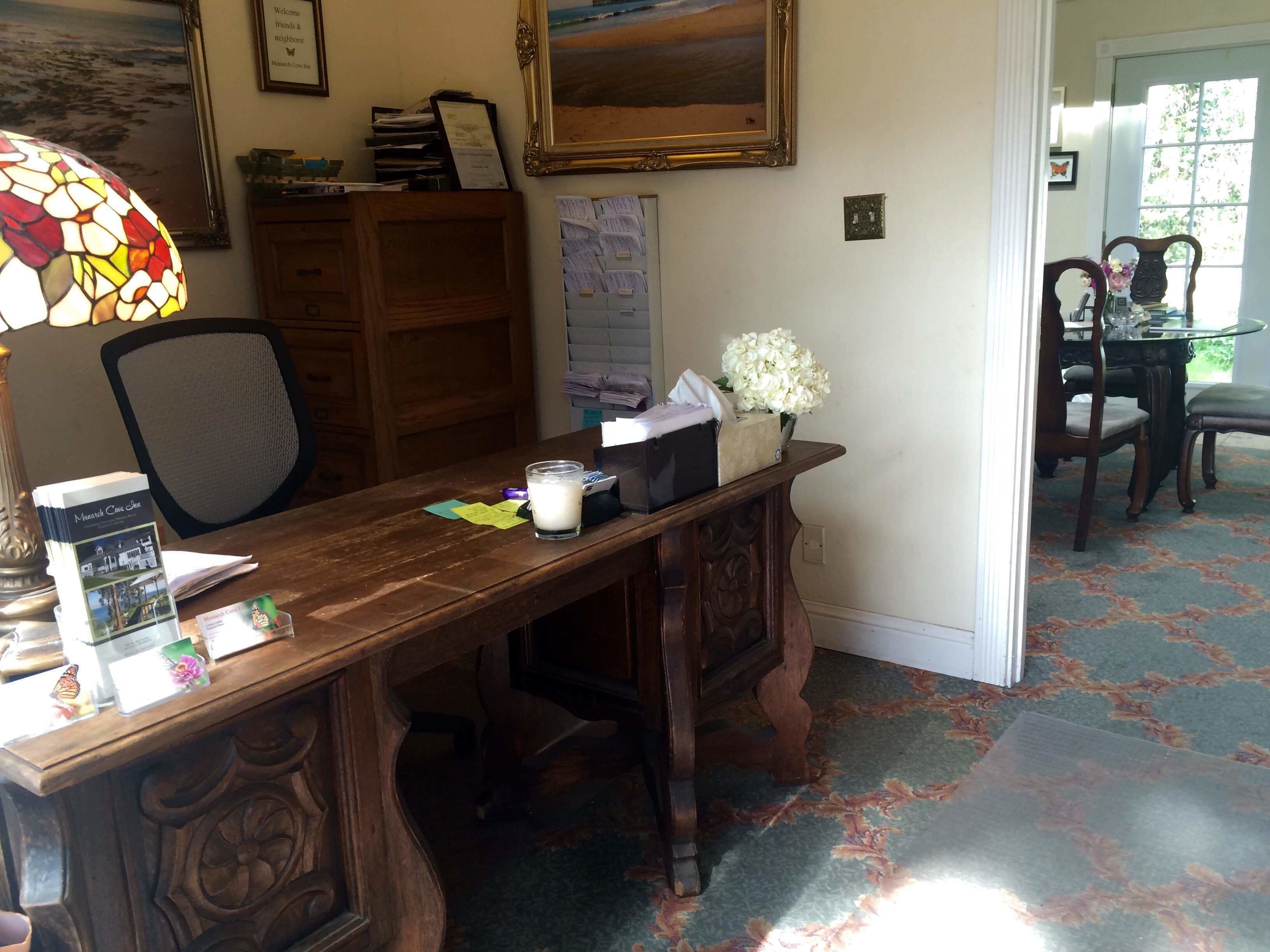 A wooden desk with a lamp, a framed painting, and a vase with flowers.