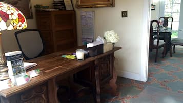 A wooden desk with a lamp, a framed painting, and a vase with flowers.