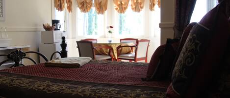 Une chambre avec un grand lit, une table à manger avec des chaises, un lustre et des rideaux.