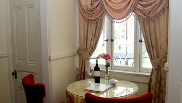 Um quarto com uma mesa redonda, duas cadeiras vermelhas, uma garrafa de vinho, uma taça de vinho e um vaso com flores.