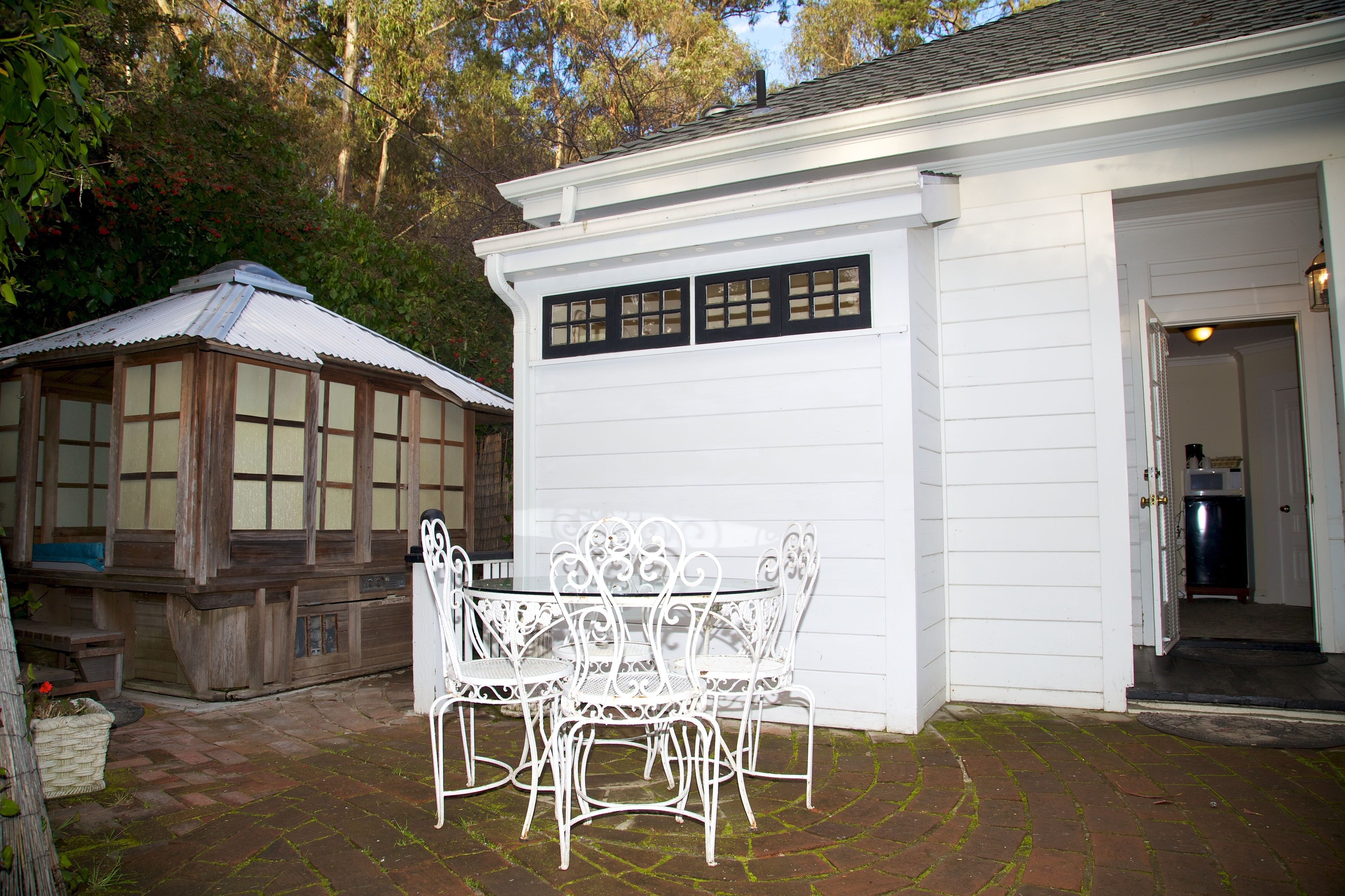 A white building with a garage door, a patio with a table and chairs, and a wooden structure with windows.