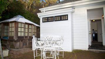 A white building with a garage door, a patio with a table and chairs, and a wooden structure with windows.