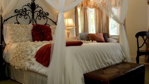 A bedroom with a four-poster bed, a nightstand, a lamp, and a chair.