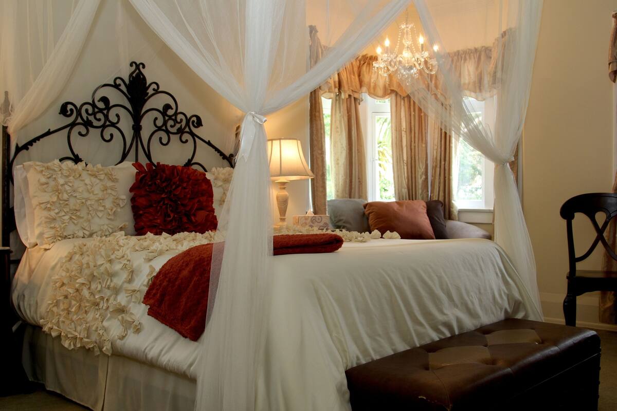 A bedroom with a four-poster bed, a nightstand, a lamp, and a chair.