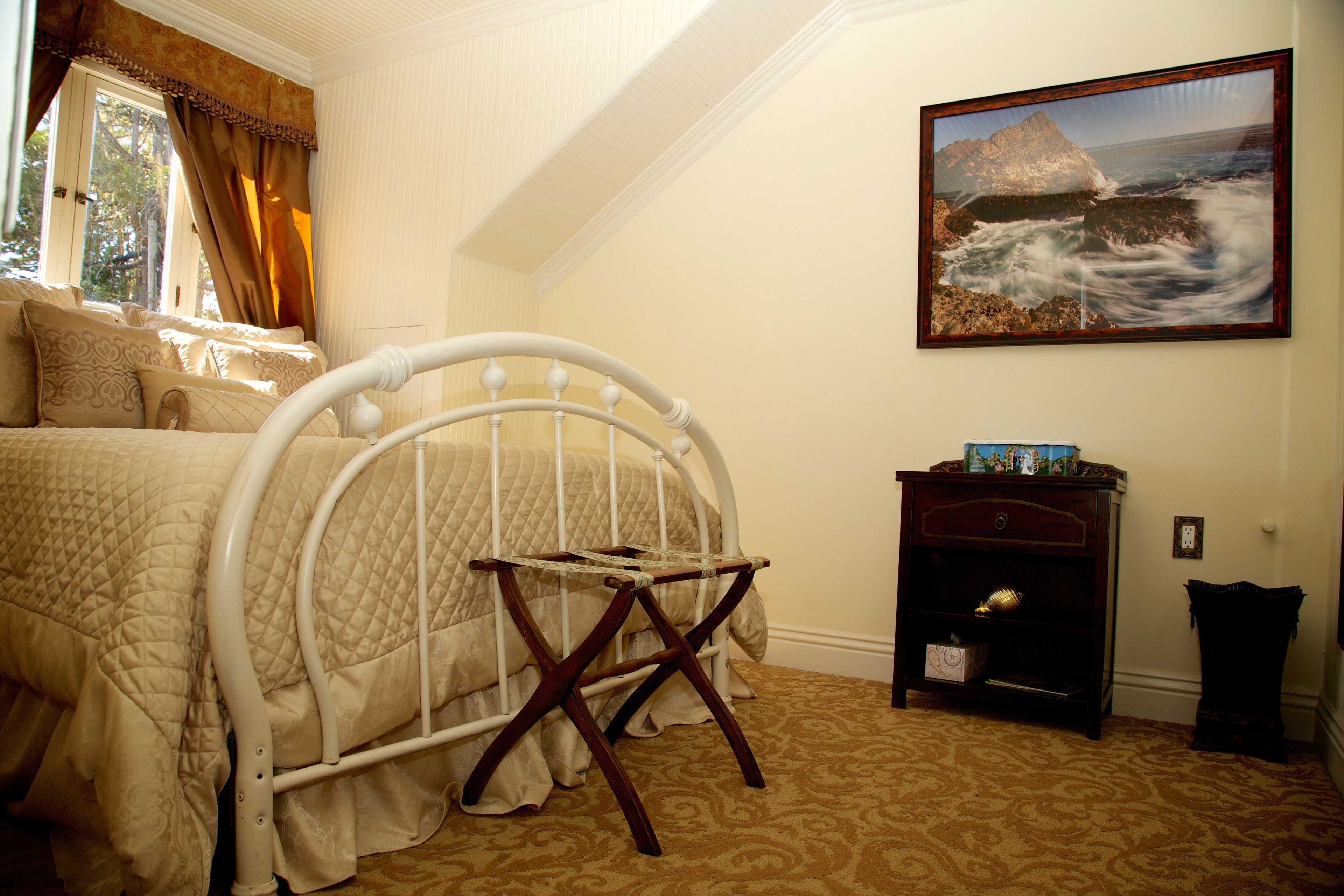 A bedroom with a bed, a wooden chair, a painting, and a nightstand.