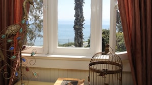 A room with a window overlooking the sea, a decorative peacock, and a birdcage. - Monarch Cove Inn (Capitola)