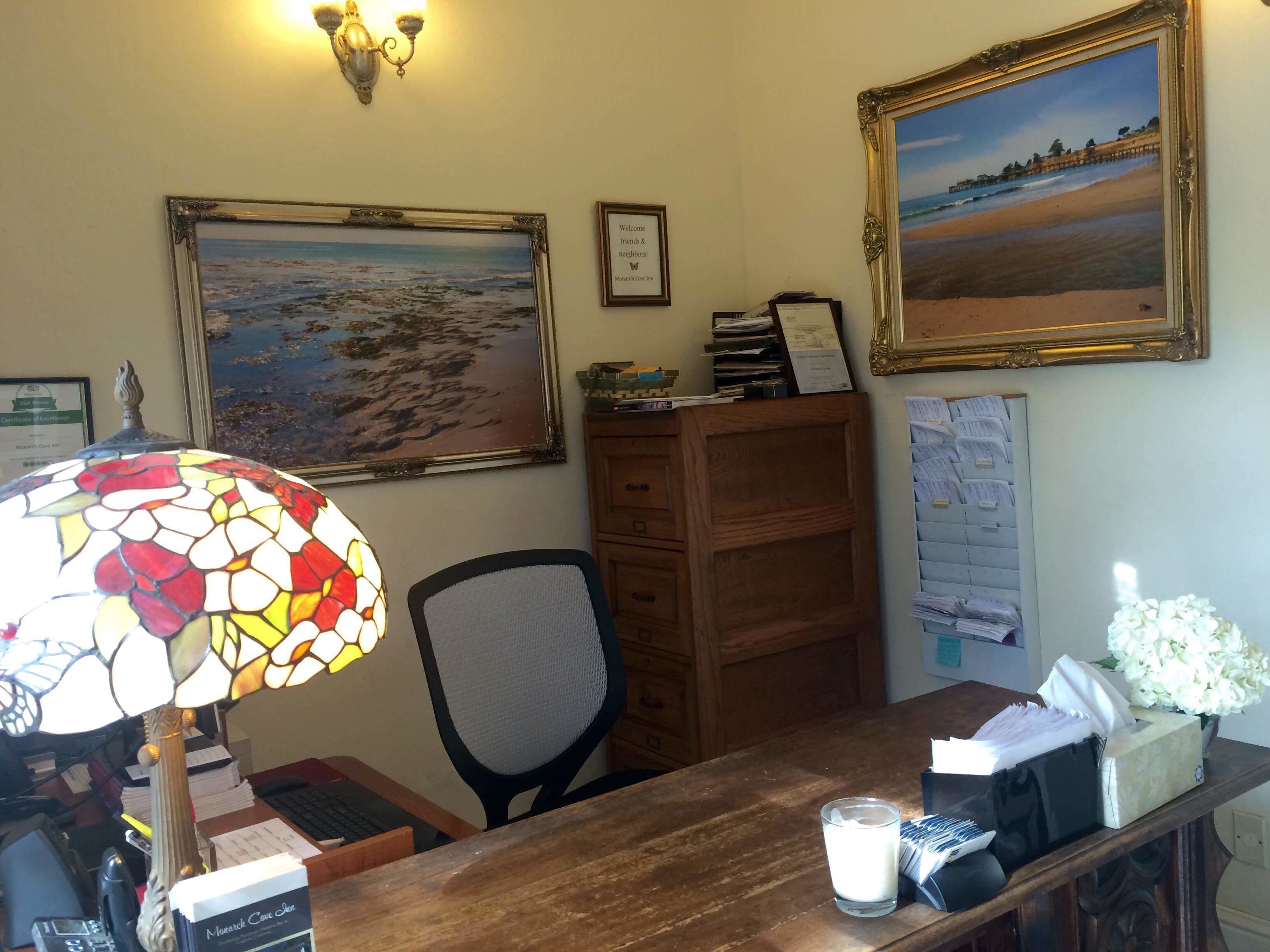 A desk with a stained glass lamp, a framed painting of a beach, and a wooden cabinet.