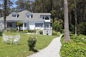 A two-story white house with a covered patio, a lawn, and a pathway leading to the house.