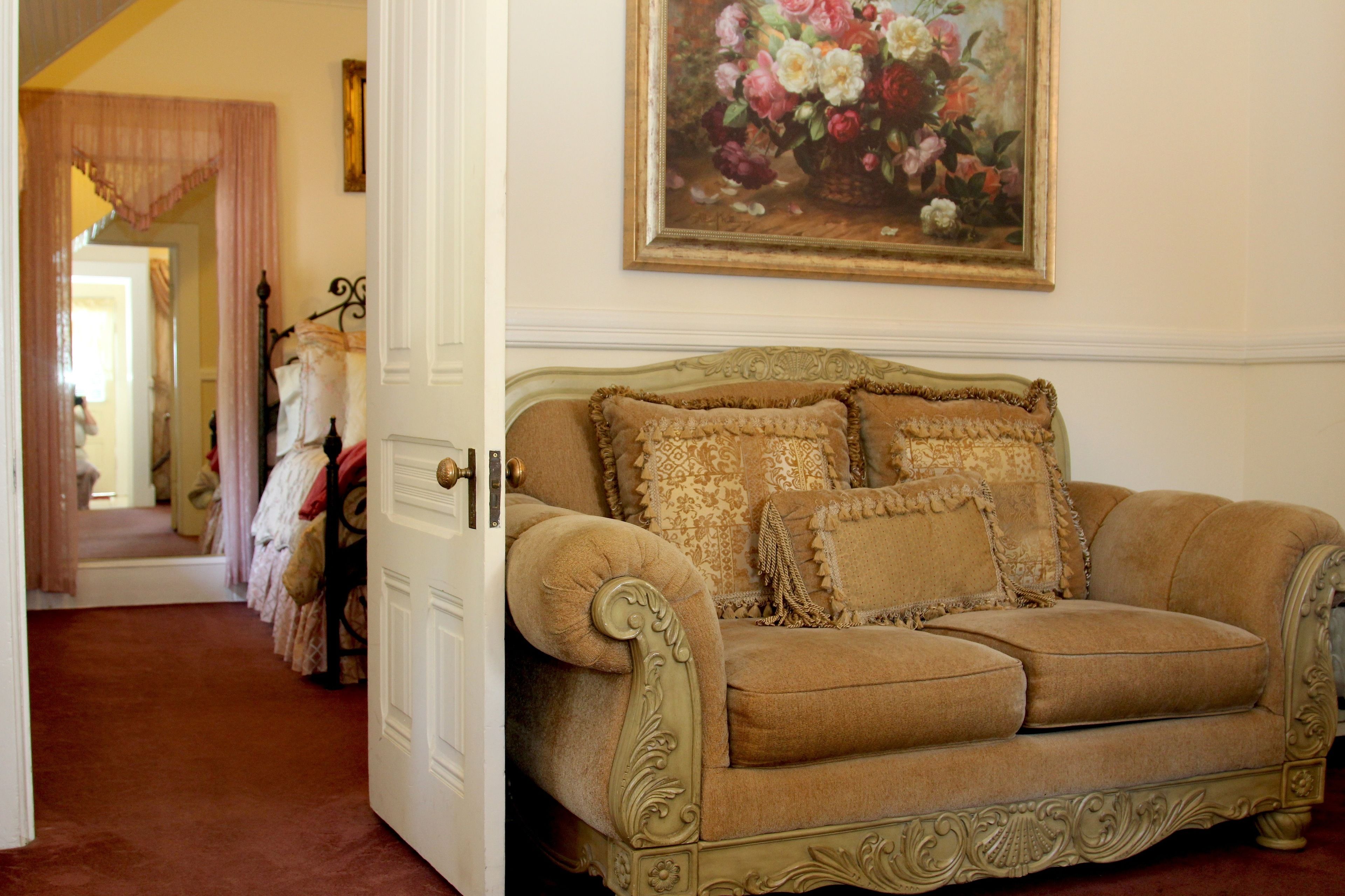 Ein Sofa im Vintage-Stil mit aufwendiger Verzierung, ein Blumenbild an der Wand und ein Flur mit Spiegel und Kleiderständer.