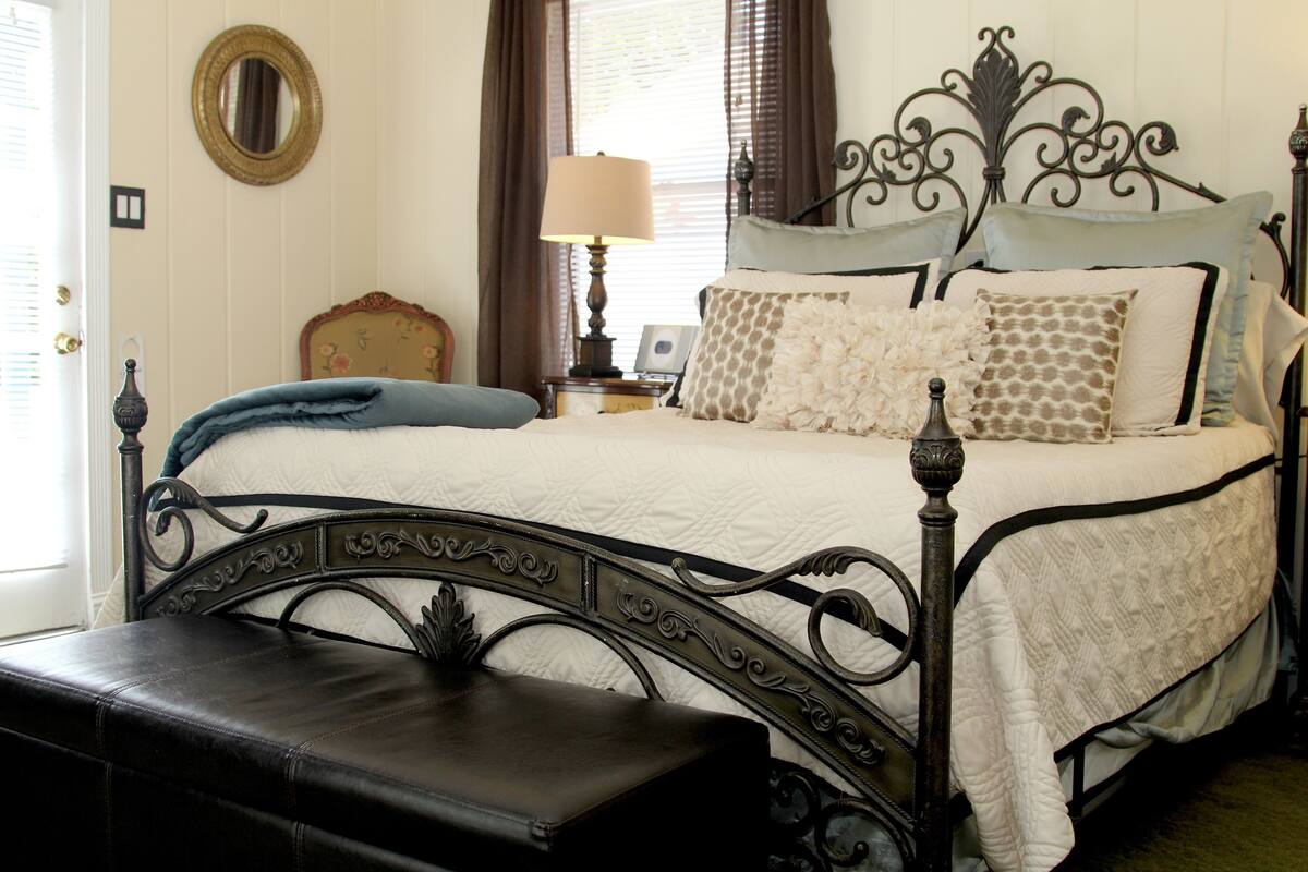A neatly made bed with a headboard, a bedside table with a lamp, and a bench at the foot of the bed.