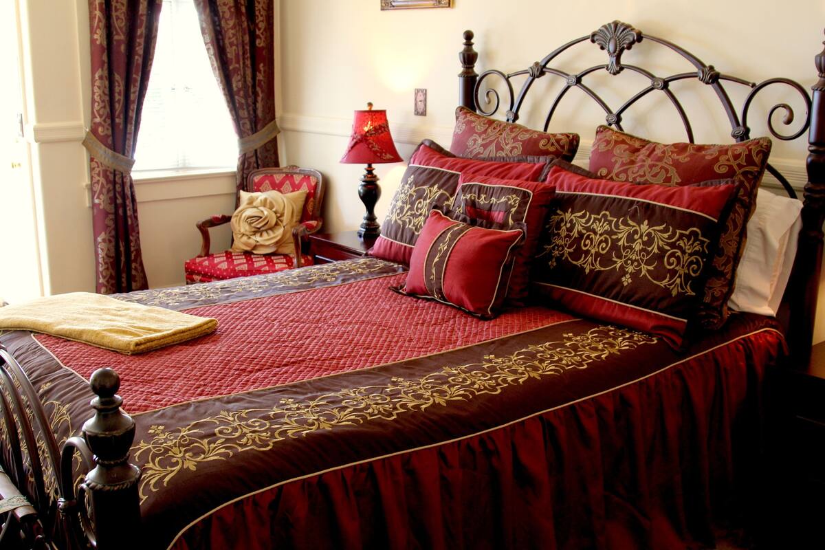 A bed with a red and brown bedspread, a wooden headboard, and multiple pillows.