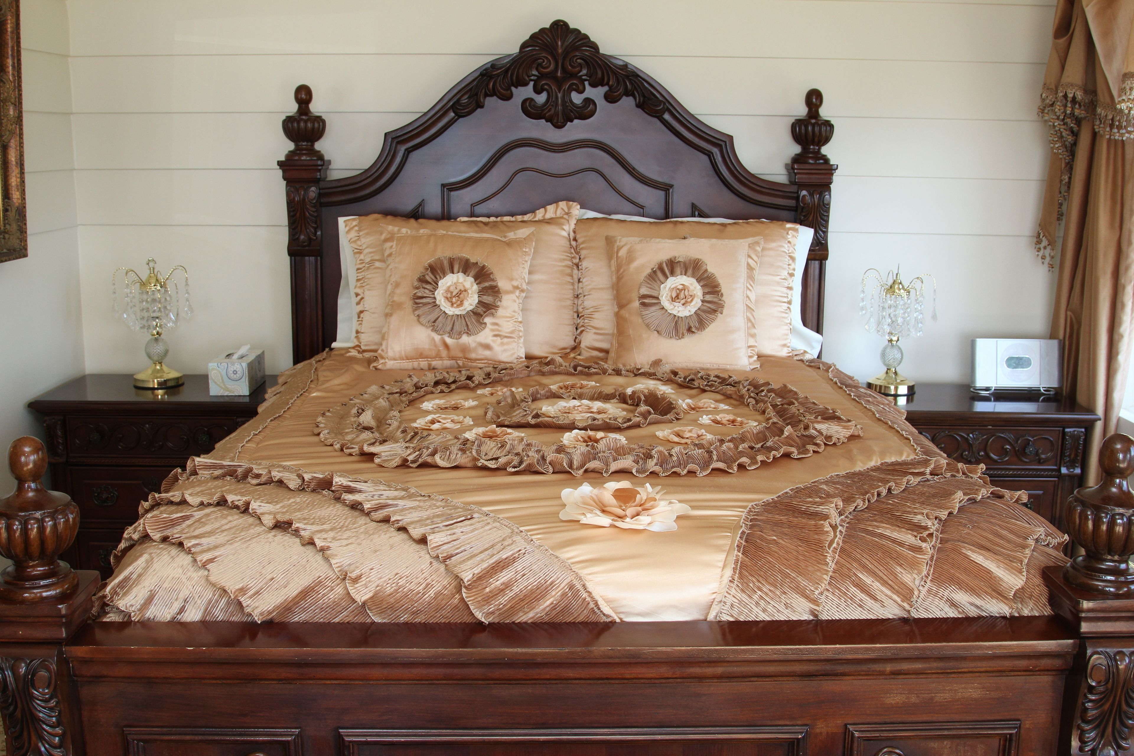 A bed with a ruffled bedspread and decorative pillows, wooden headboard, and matching nightstands with lamps.