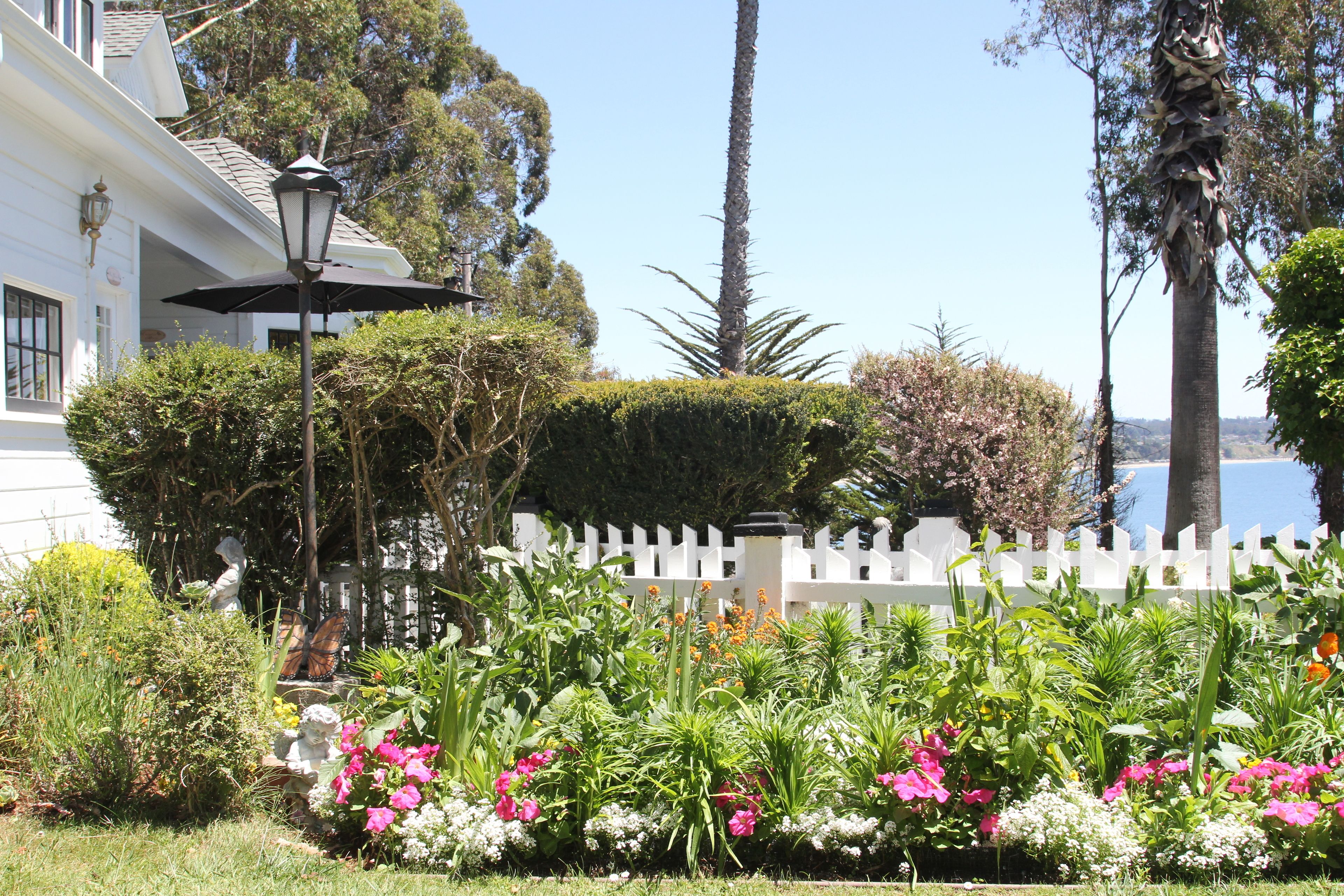Um jardim com diversas plantas e flores, um cercado branco e um poste de luz.