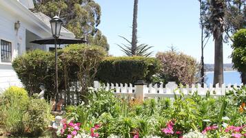 Um jardim com diversas plantas e flores, um cercado branco e um poste de luz.