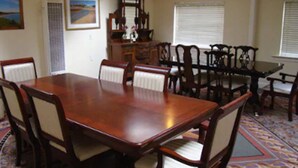 A dining room with a large wooden table surrounded by chairs, a window with blinds, and a decorative rug.